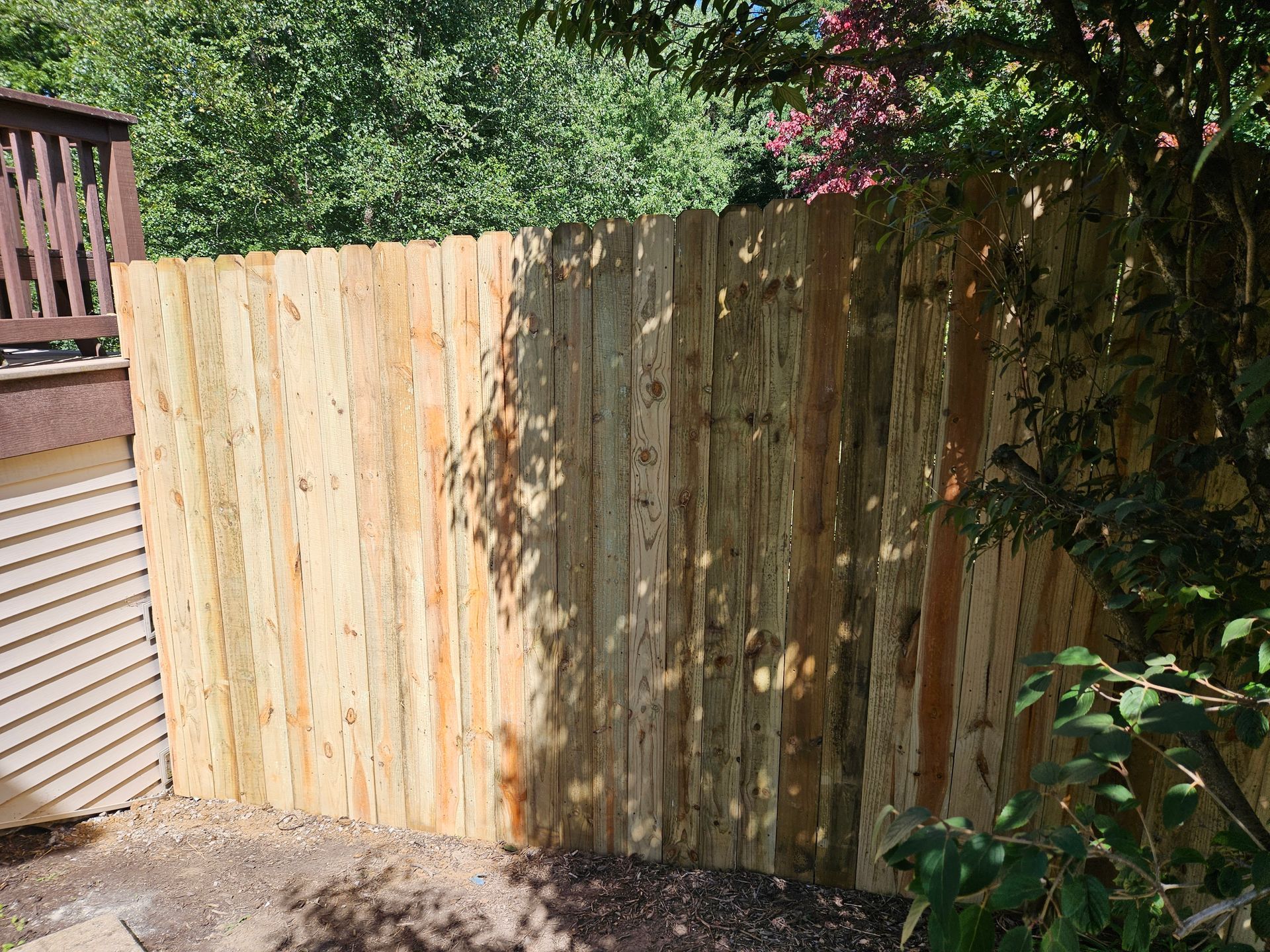 Wooden privacy fence in a backyard, with a deck and greenery visible.