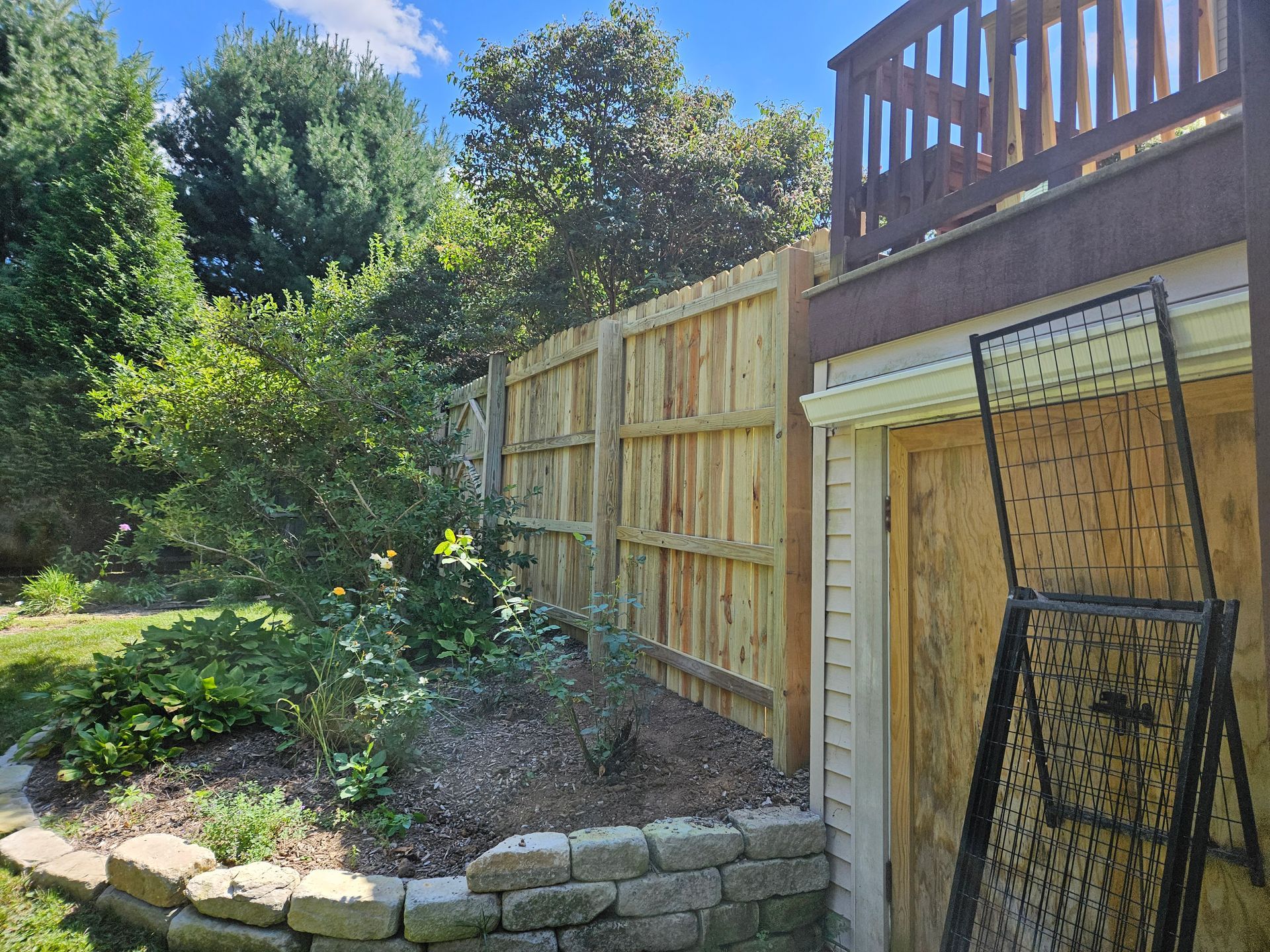 Wooden fence beside a building and garden on a sunny day.