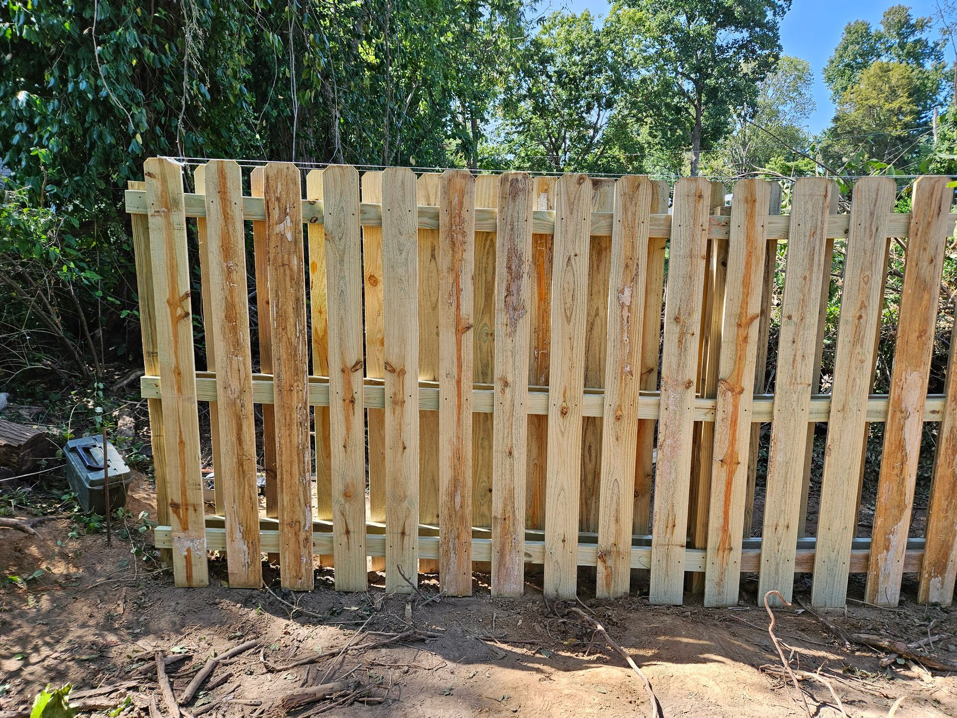 Wooden picket fence in a natural setting, trees in the background.