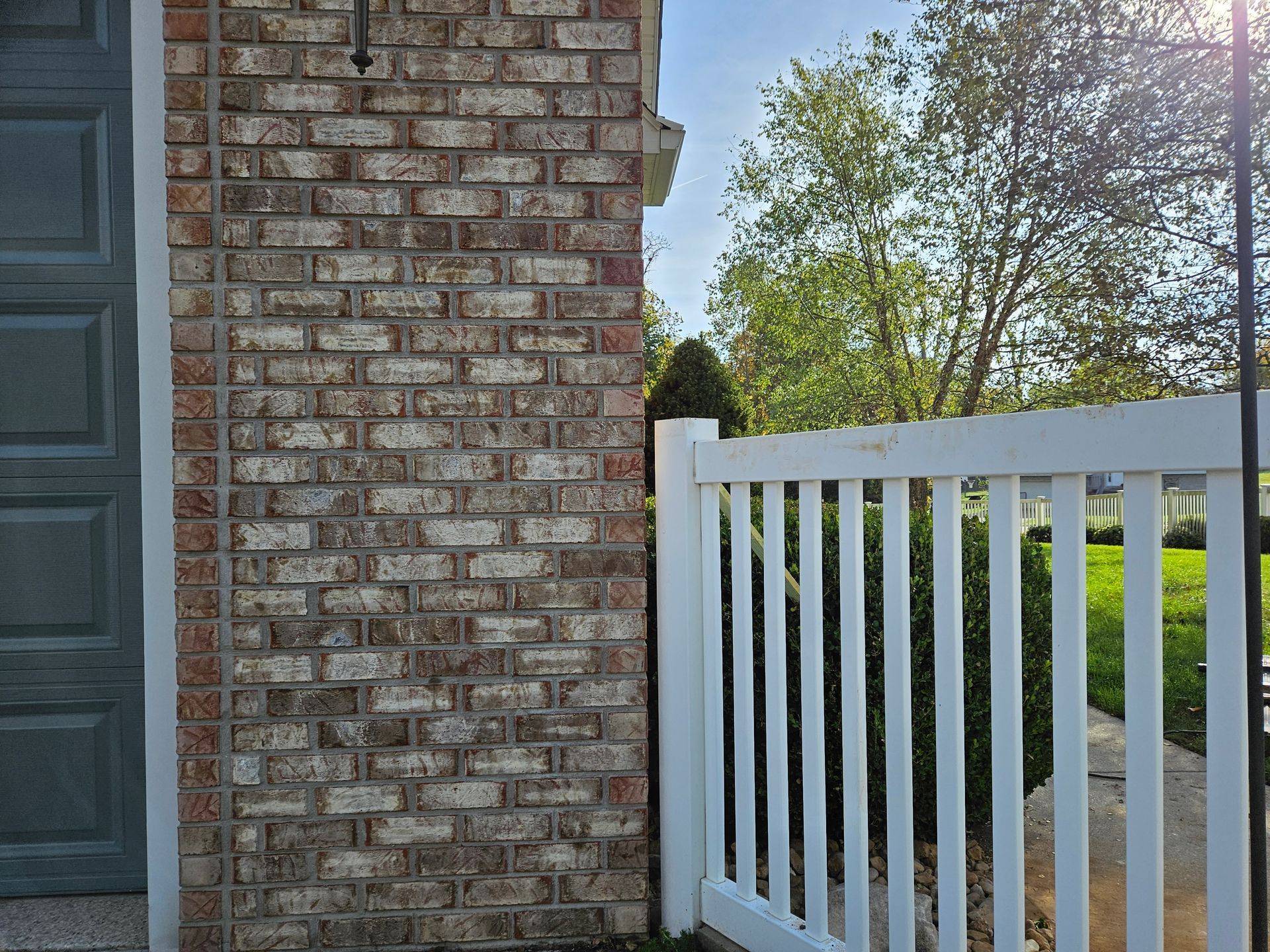 Brick wall next to a white picket fence, a gray door is on the left.