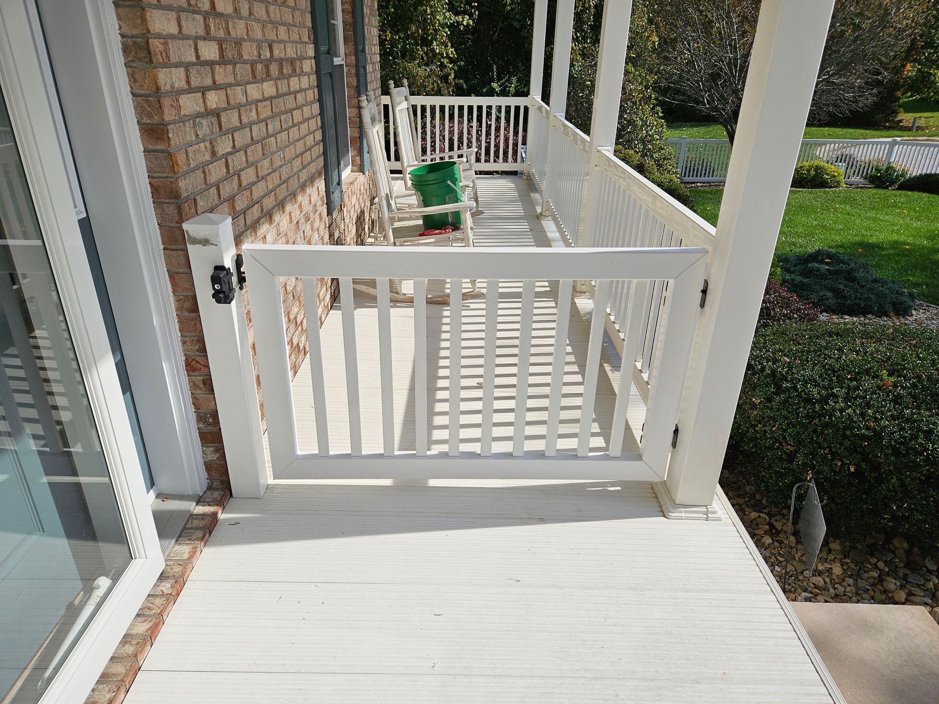 White gate on a porch. White railing surrounds the porch with a view of a grassy lawn.