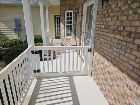 White porch with railing and gate next to a brick wall.