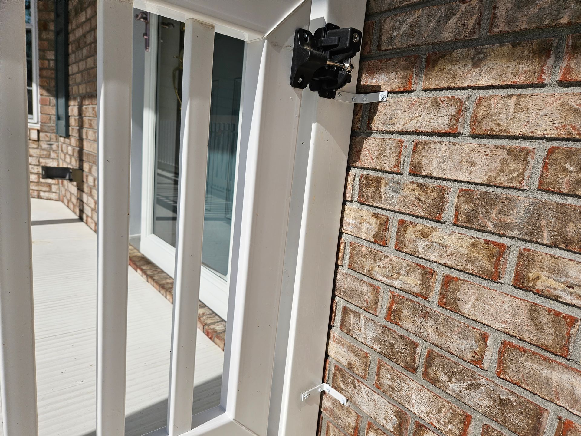 Black security camera mounted on a white porch railing next to a brick wall.