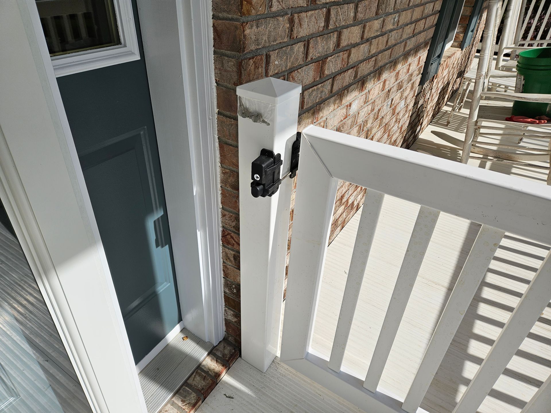 White gate latch on a porch post next to a brick wall and a blue door.