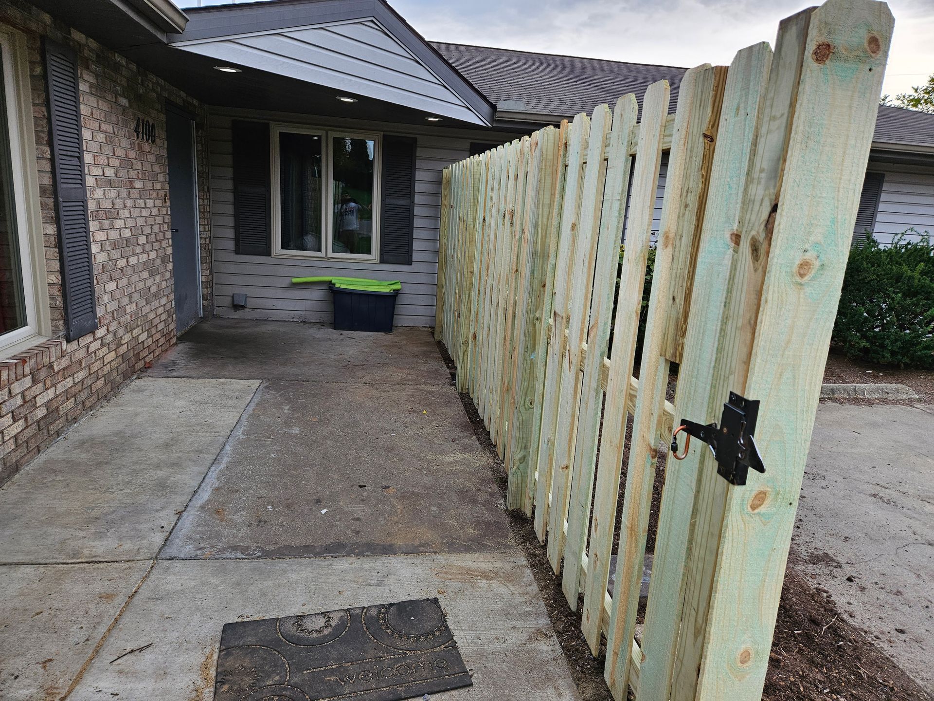 Newly built wooden fence along a concrete walkway in front of a house.