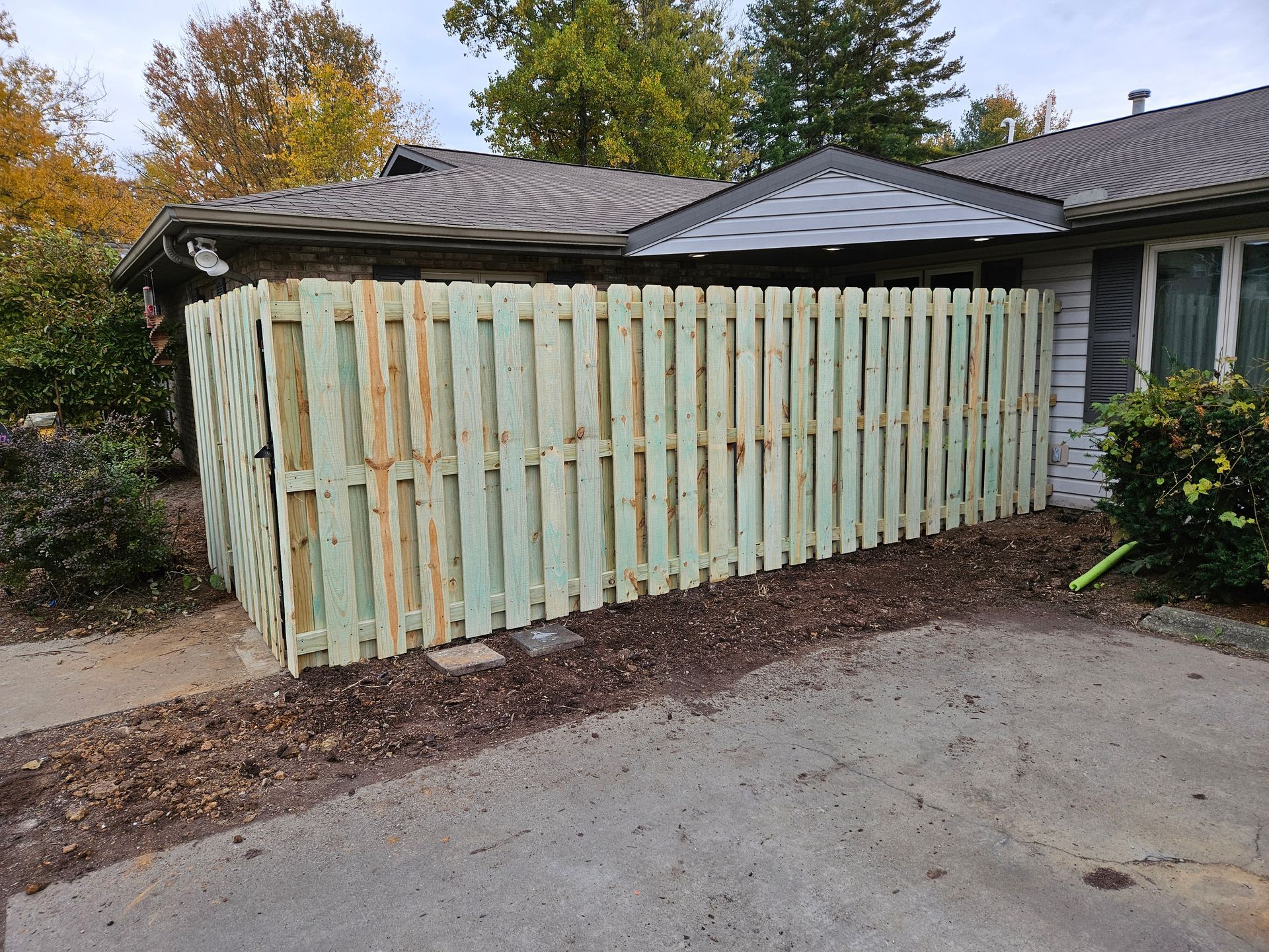 Wooden fence alongside a house; the fence is light green, the house is brown.
