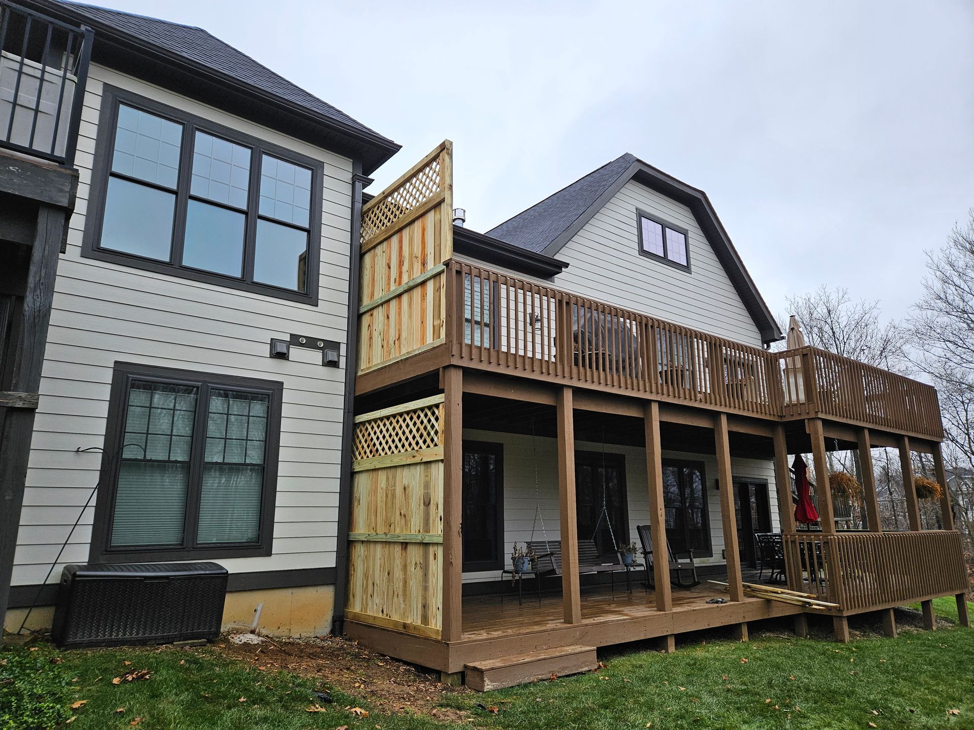 Two-story wooden deck attached to a light-colored house with dark trim; cloudy sky.