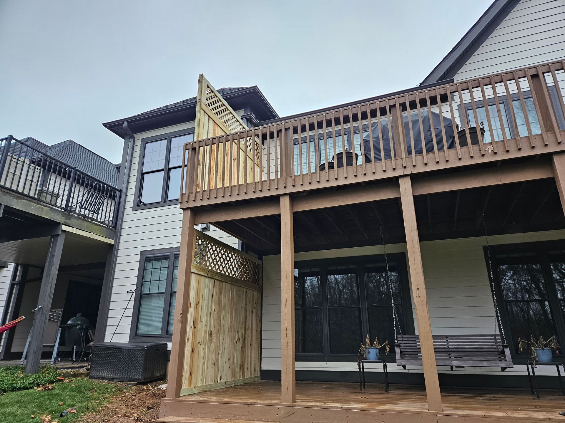Two-story house with decks. Wooden deck on top, partially covered. Another deck below with a wooden privacy screen.