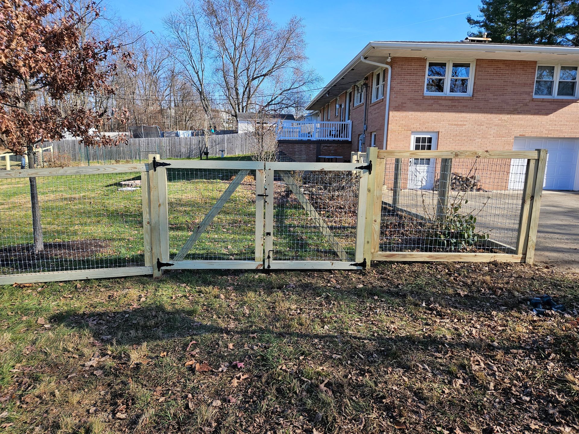 Wooden fence with a gate in a yard, in front of a brick house.