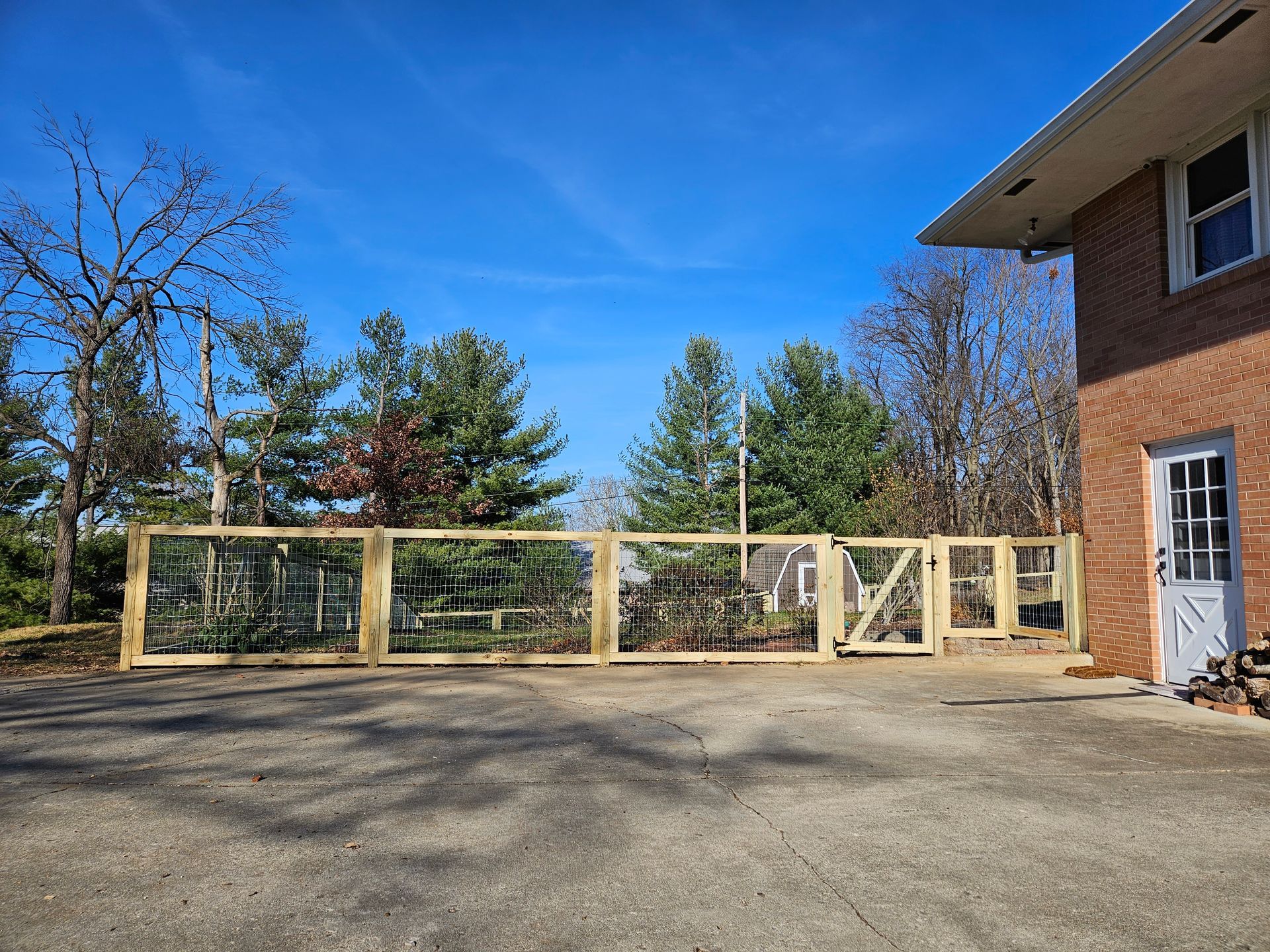 Wooden fence enclosing a yard, with a gate, next to a brick house under a blue sky.