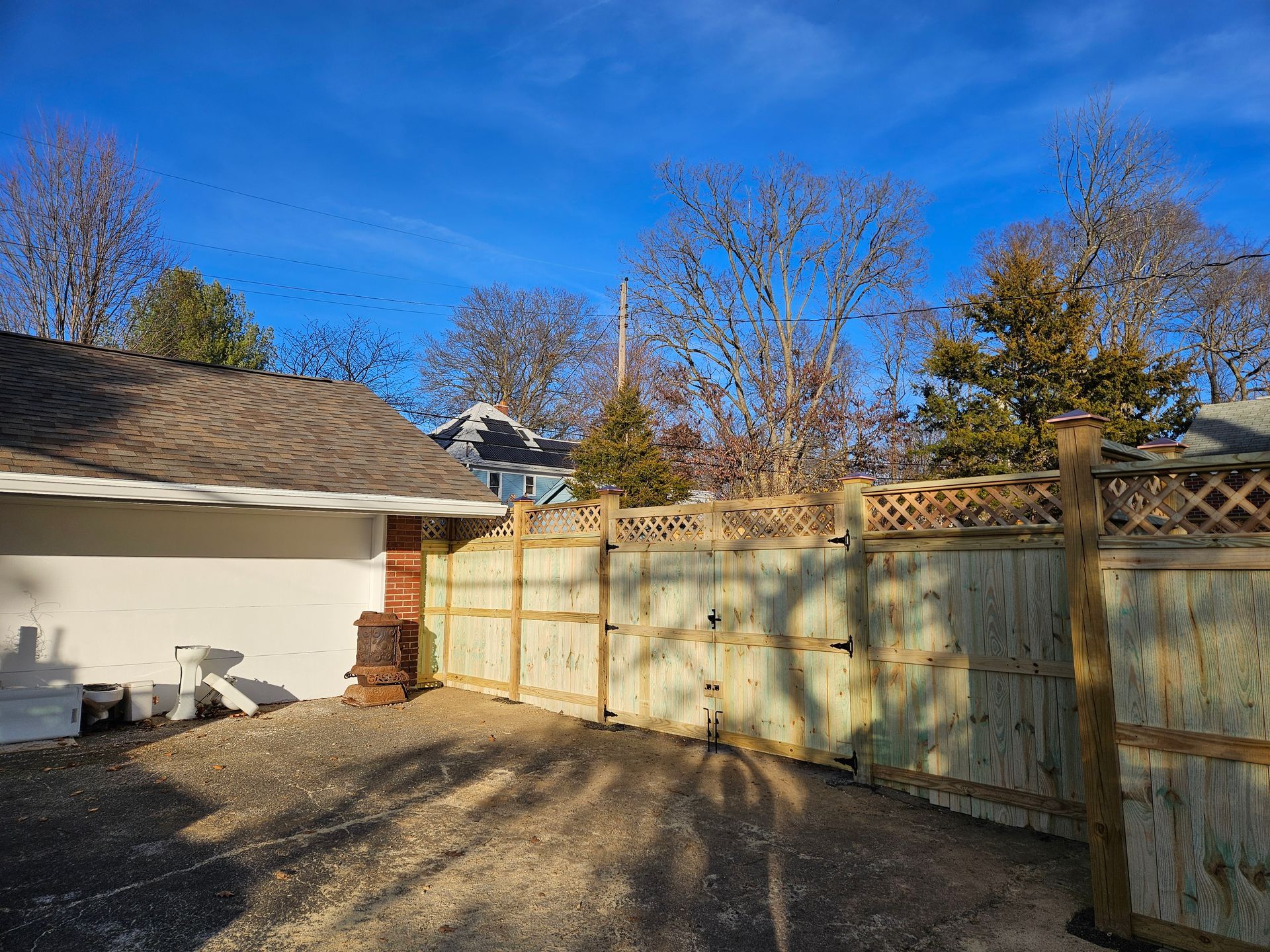 Wooden fence with lattice top, gravel driveway, and a clear blue sky.