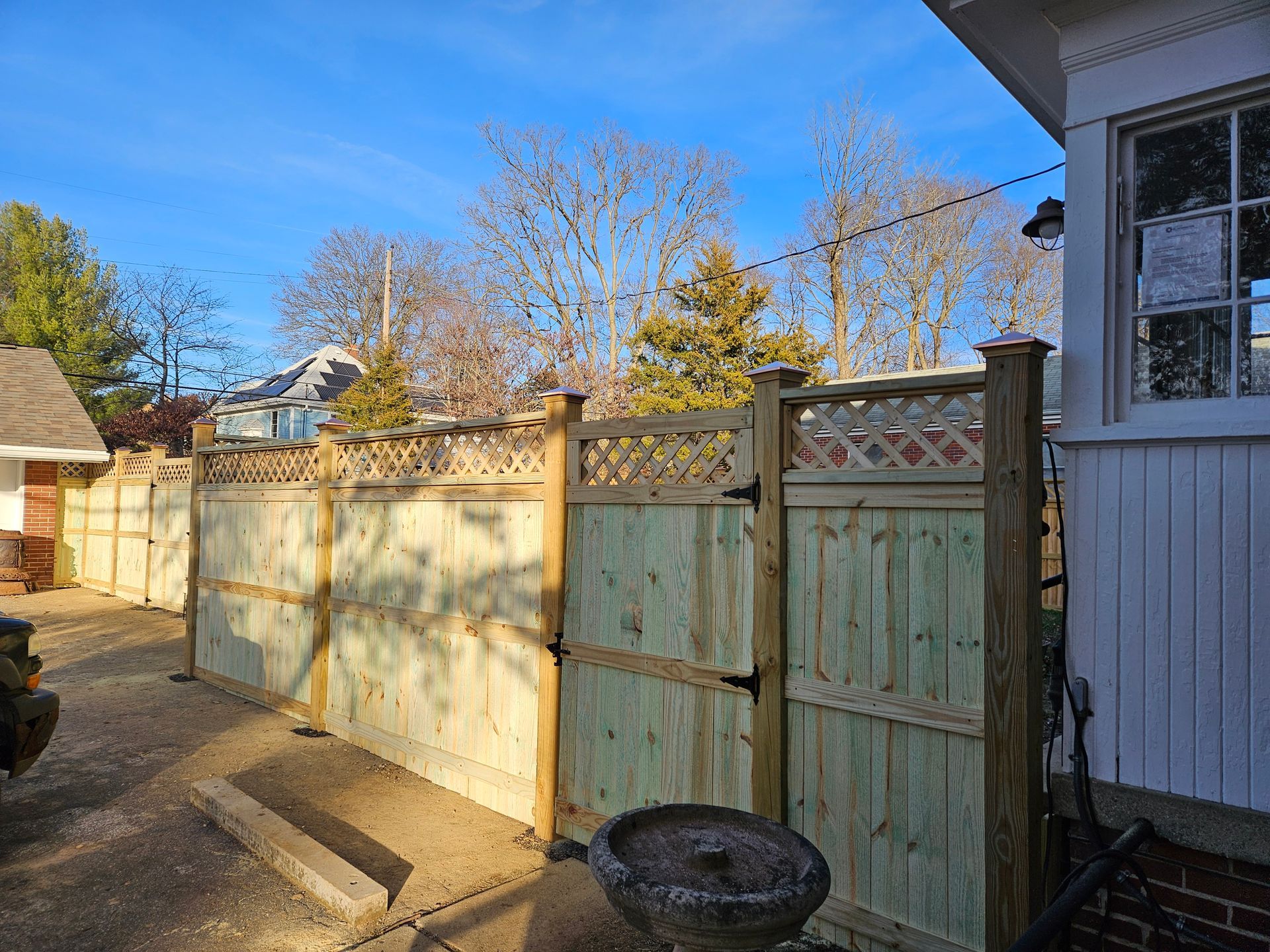 New wooden fence with lattice and gate next to a house on a sunny day.
