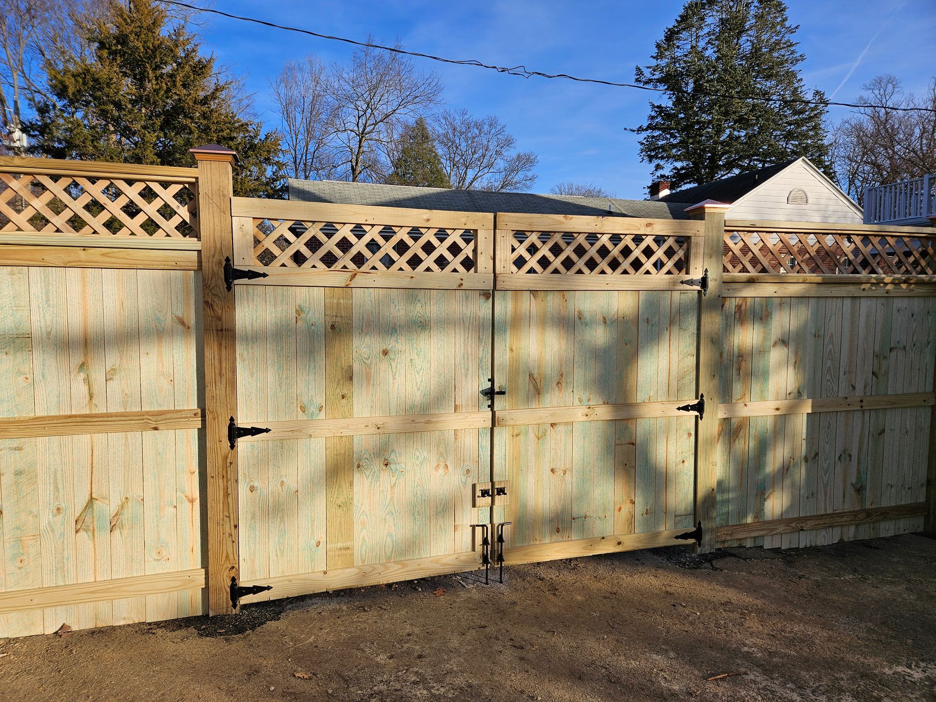 Wooden double gate with lattice top, in a sunny outdoor setting.