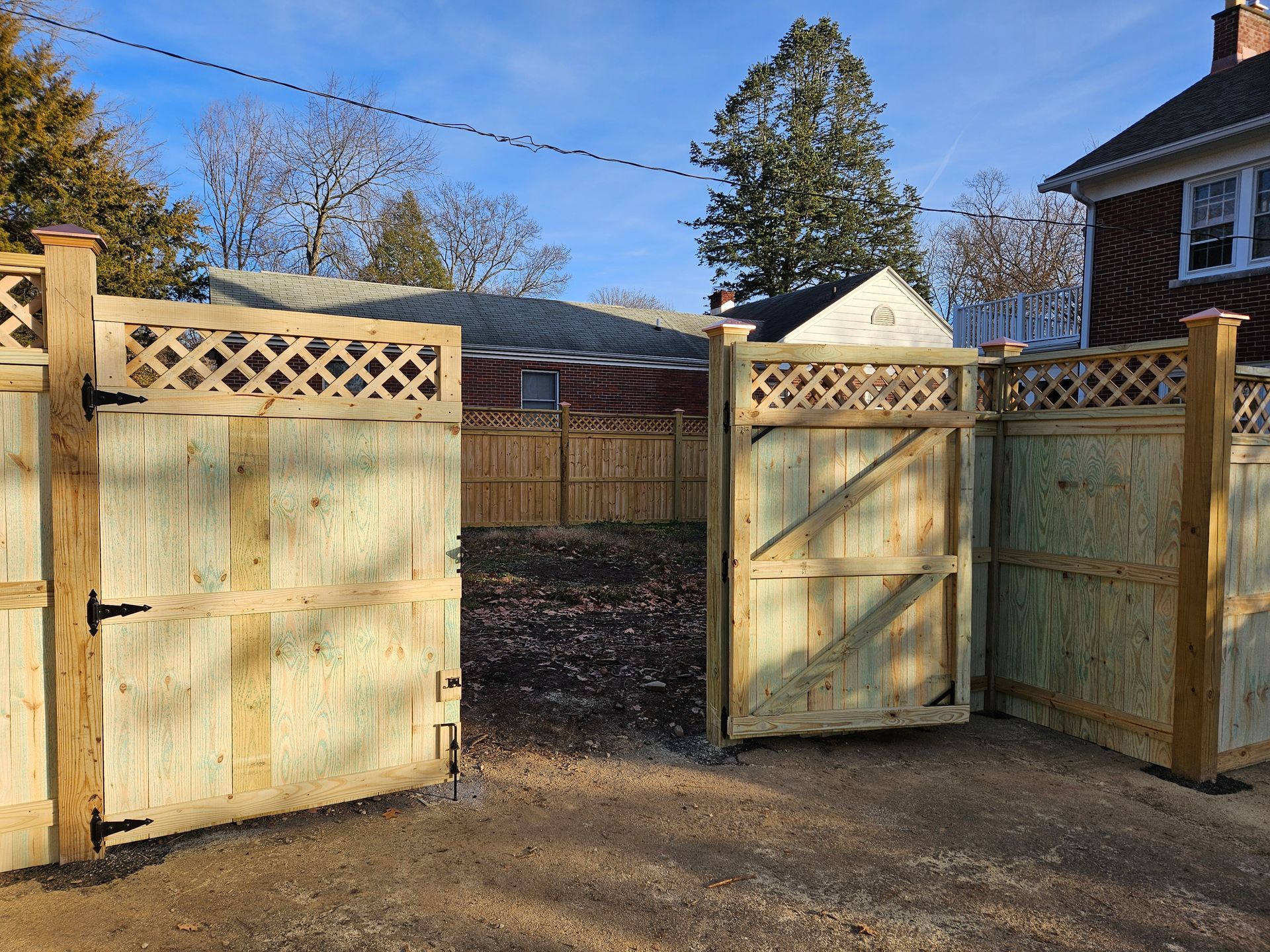 Wooden gate and fence, open. Light wood, lattice top, gravel ground. In backyard, sunny day.