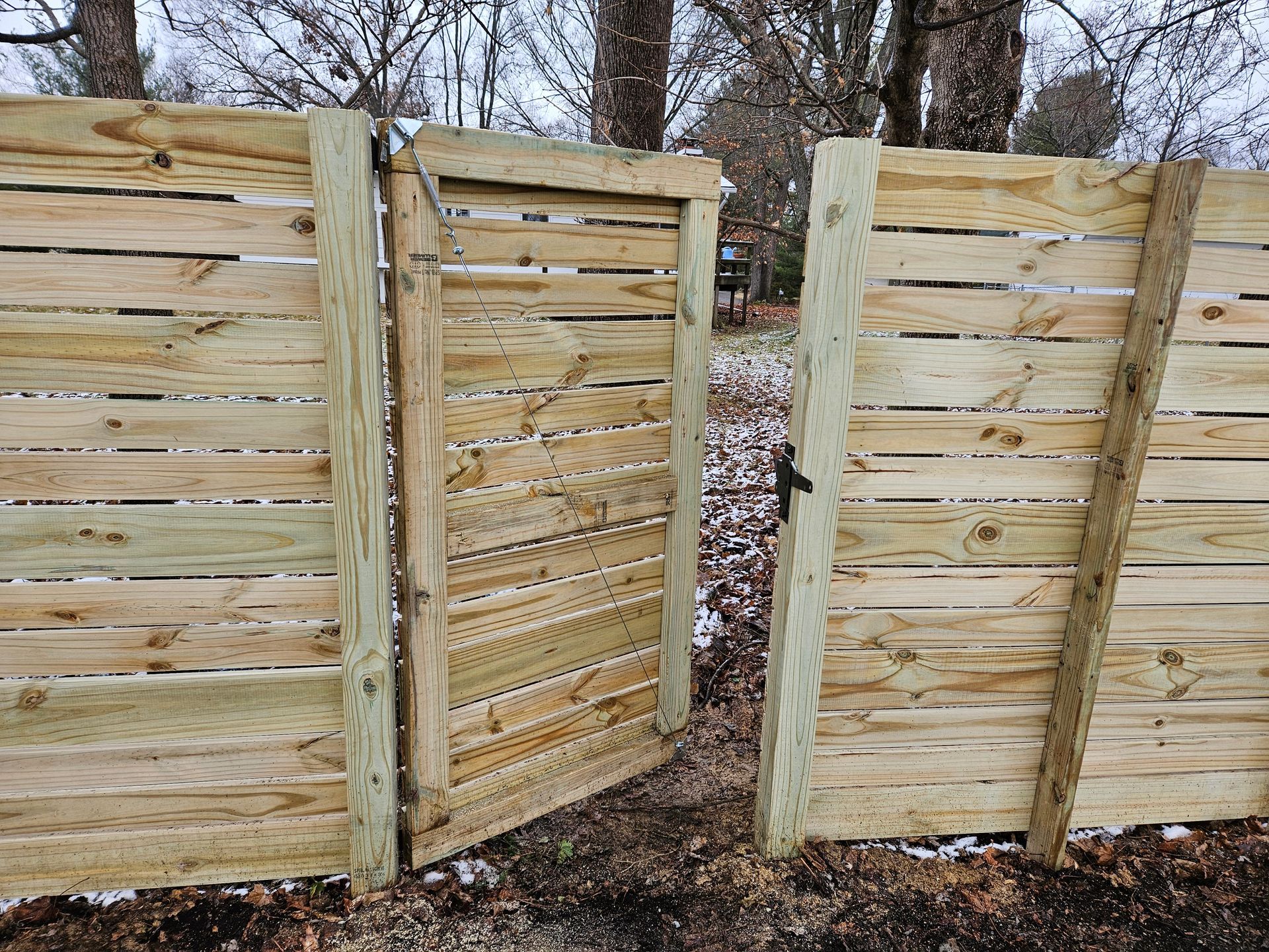 Wooden gate ajar in a horizontal plank fence. Outdoors, neutral colors, winter setting.