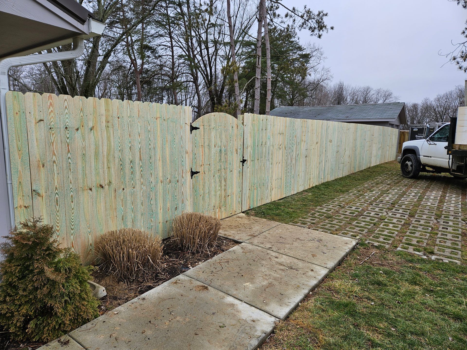 Wooden fence with gate; front yard with concrete pathway, truck parked on right.