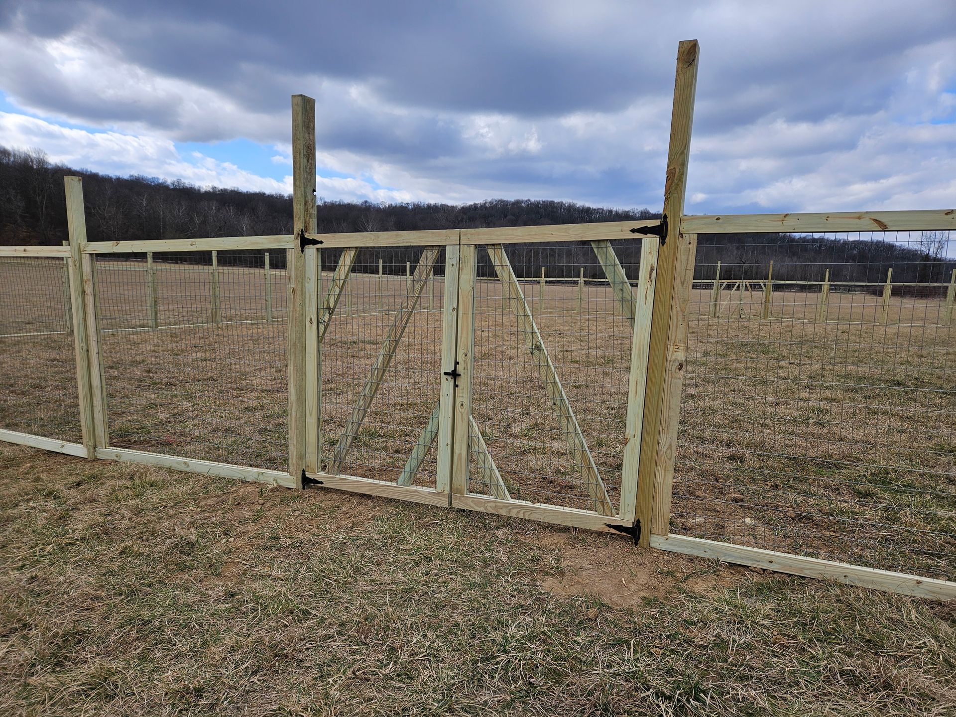 Wooden gate and fence in a field, under a cloudy sky.