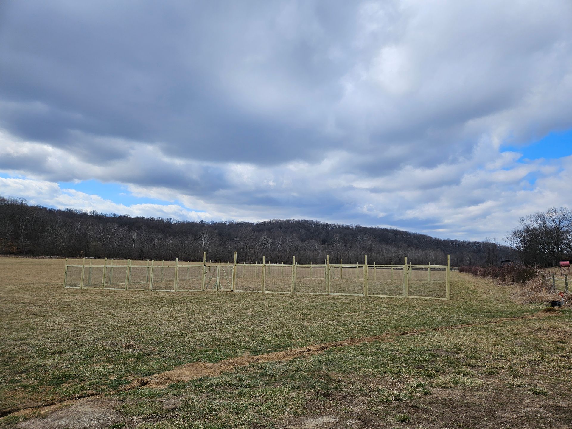 Field with a newly built wooden fence under a cloudy sky with treeline in the background.
