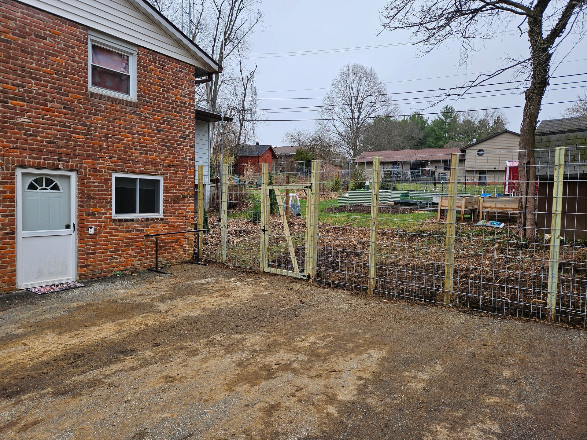 A gravel driveway with a new wooden fence in front of a brick building and garden area.