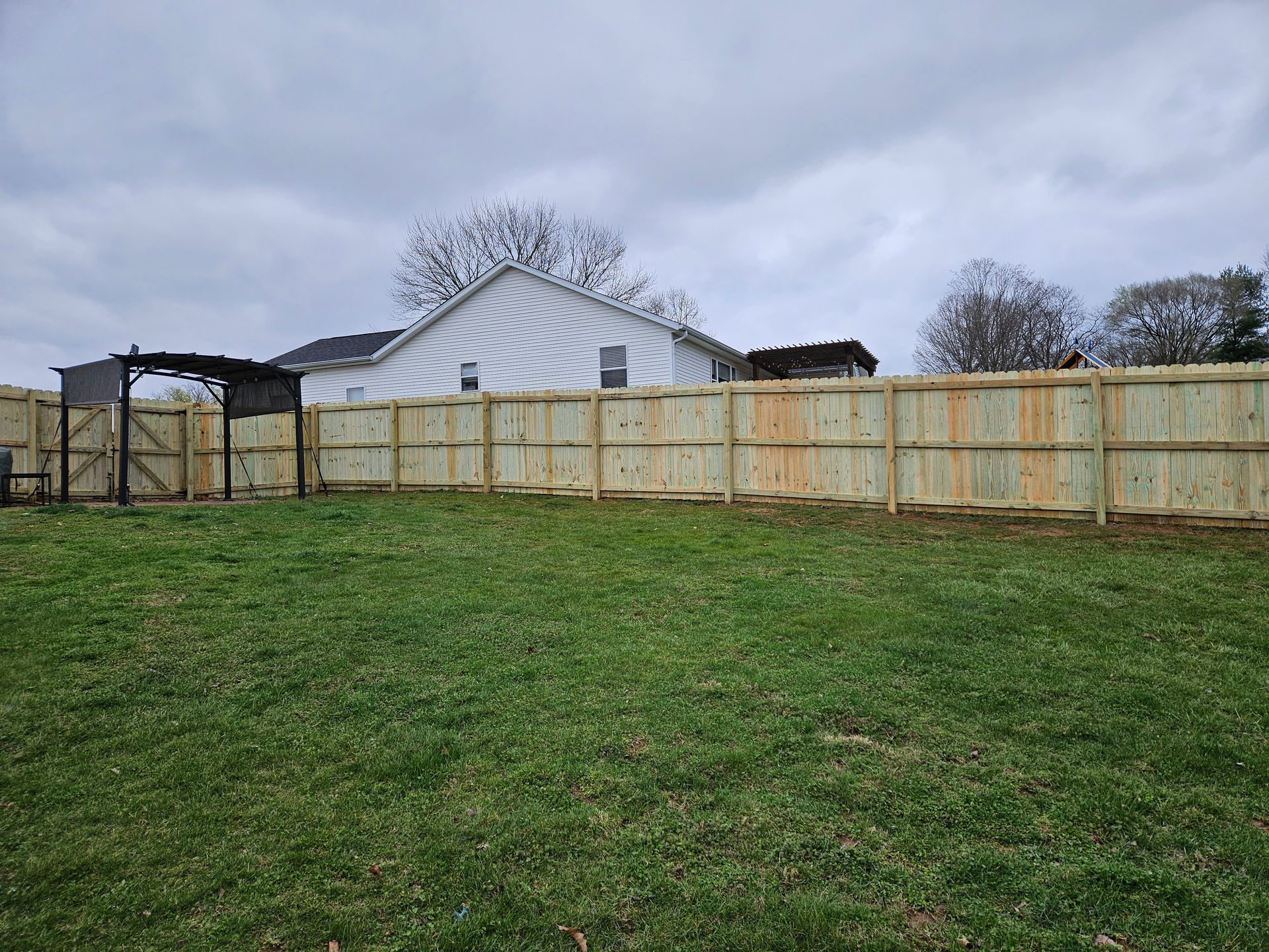 A newly built wooden fence encloses a green backyard on a cloudy day.