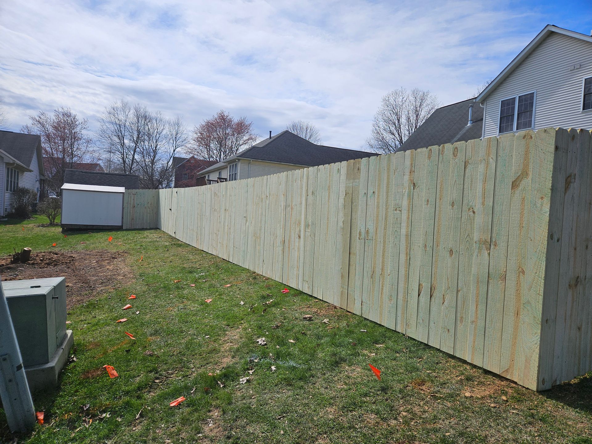 Wooden fence in backyard, spanning from left to right. Houses and sky are visible behind the fence.