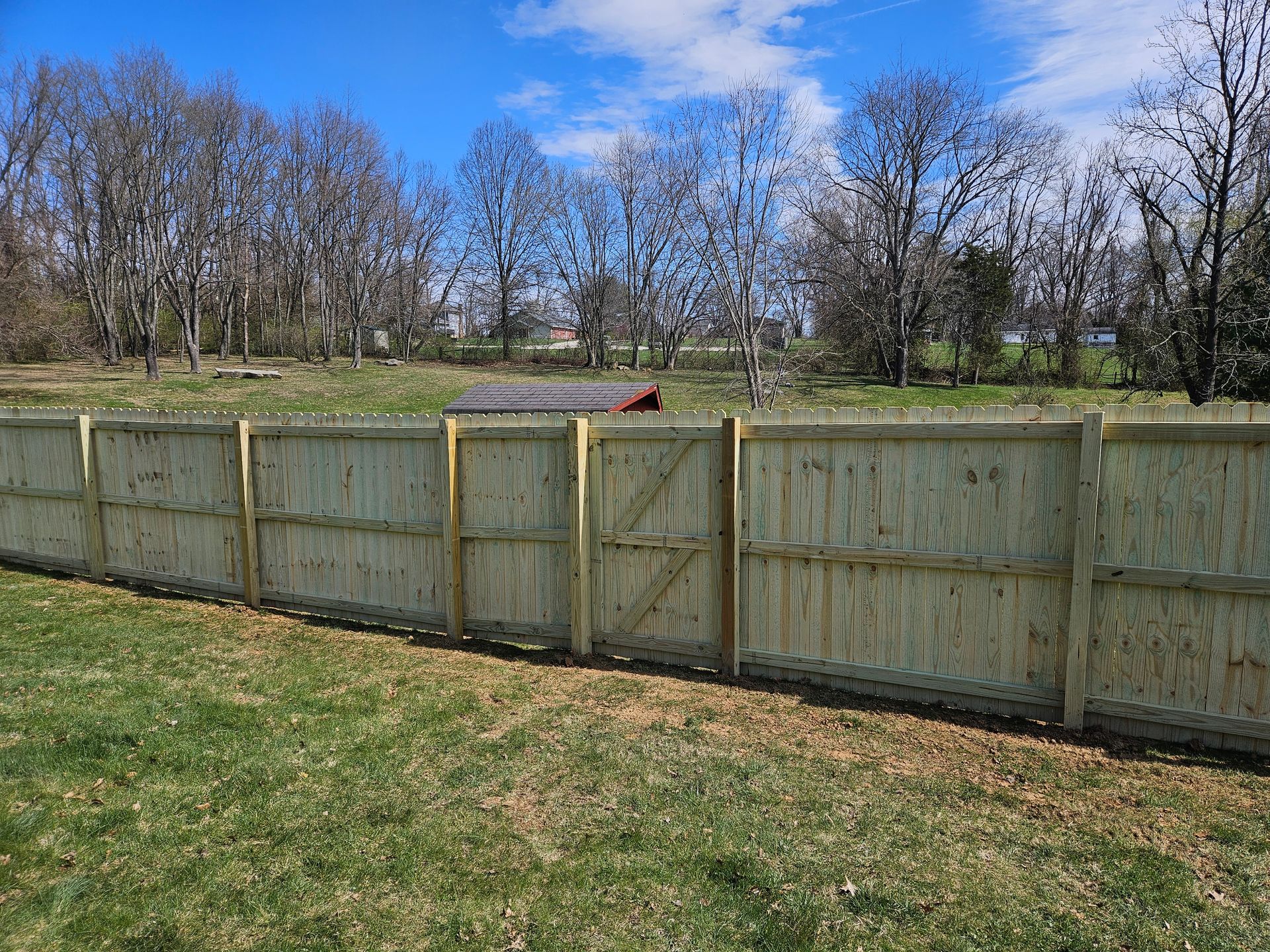 Wooden fence with gate in grassy yard, trees in background, sunny day.