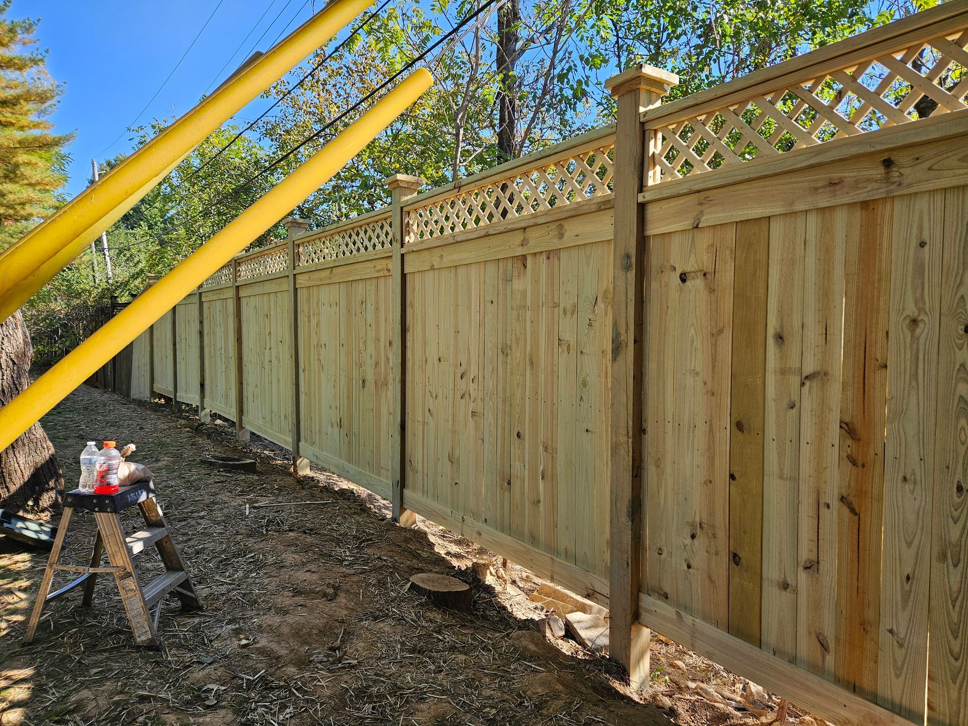 Wooden fence with lattice top, built outdoors.  Tools and materials sit nearby.