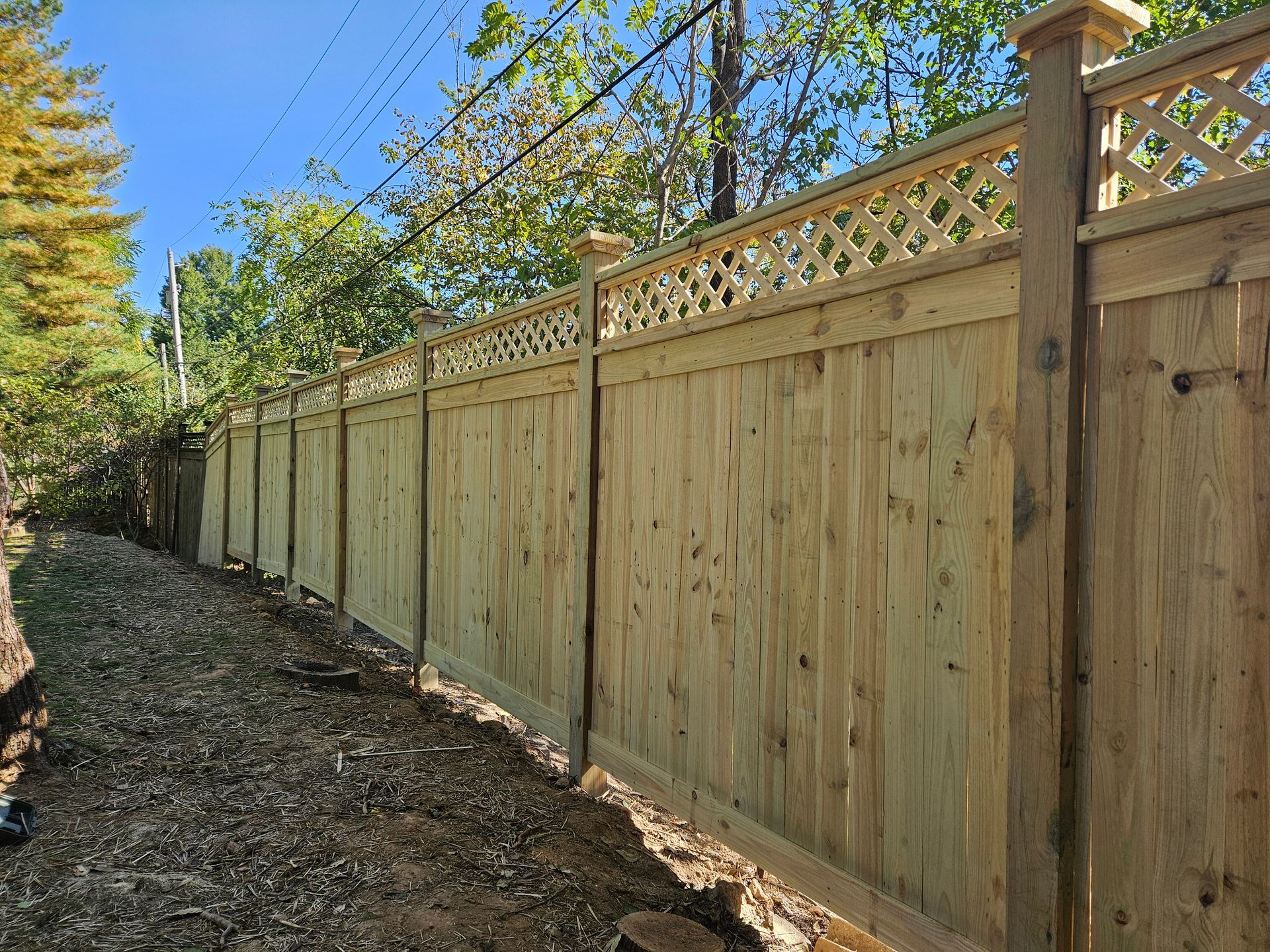 Wooden fence with lattice top running along a dirt path, under a blue sky.