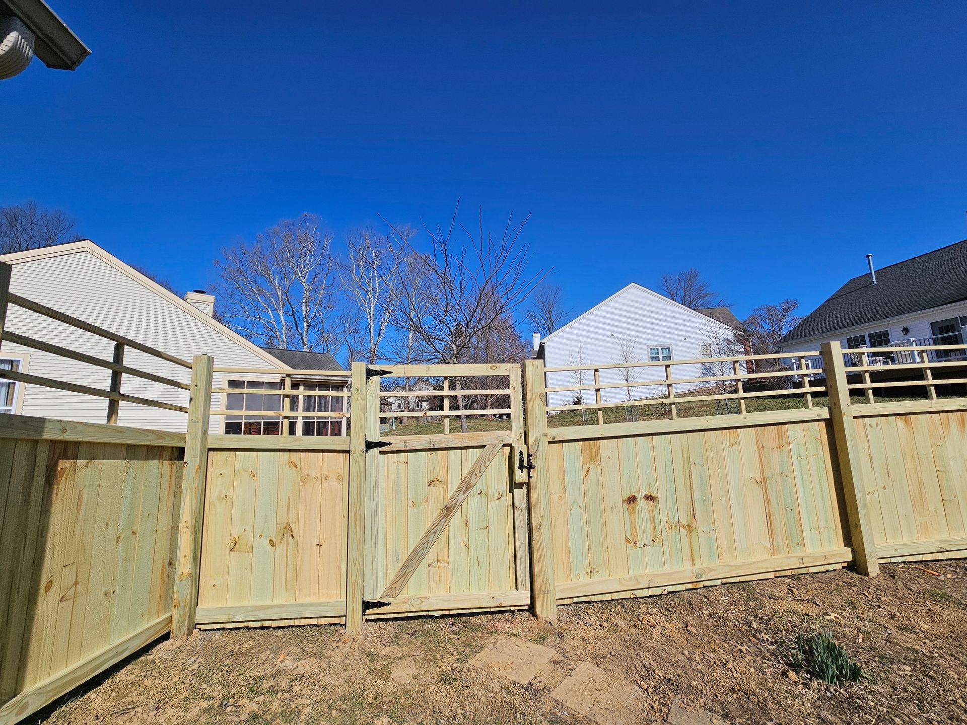 Wooden fence with gate, backyard setting. Bright blue sky overhead, houses in the background.