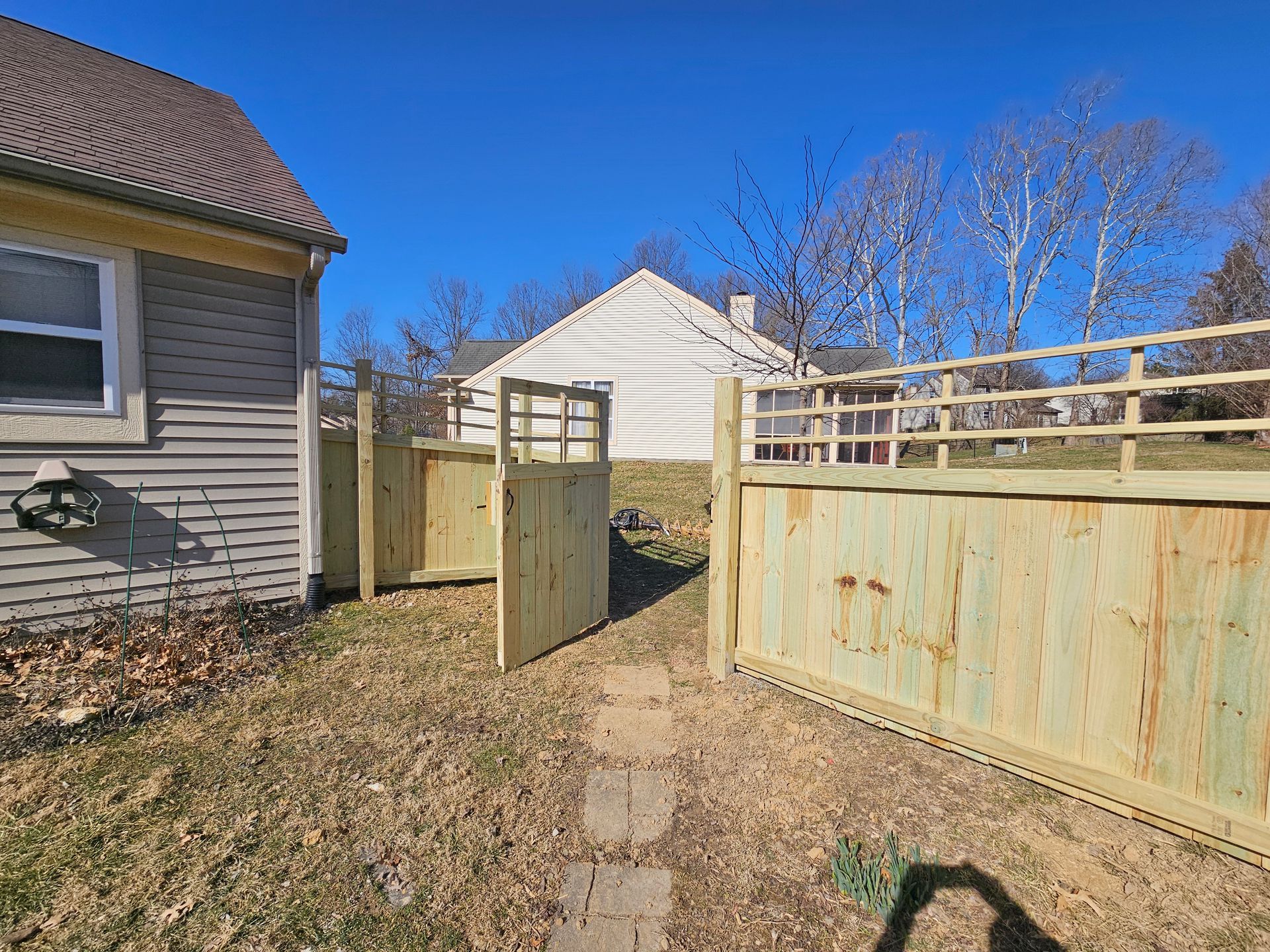Wooden fence with a gate, next to a house, sunny day.