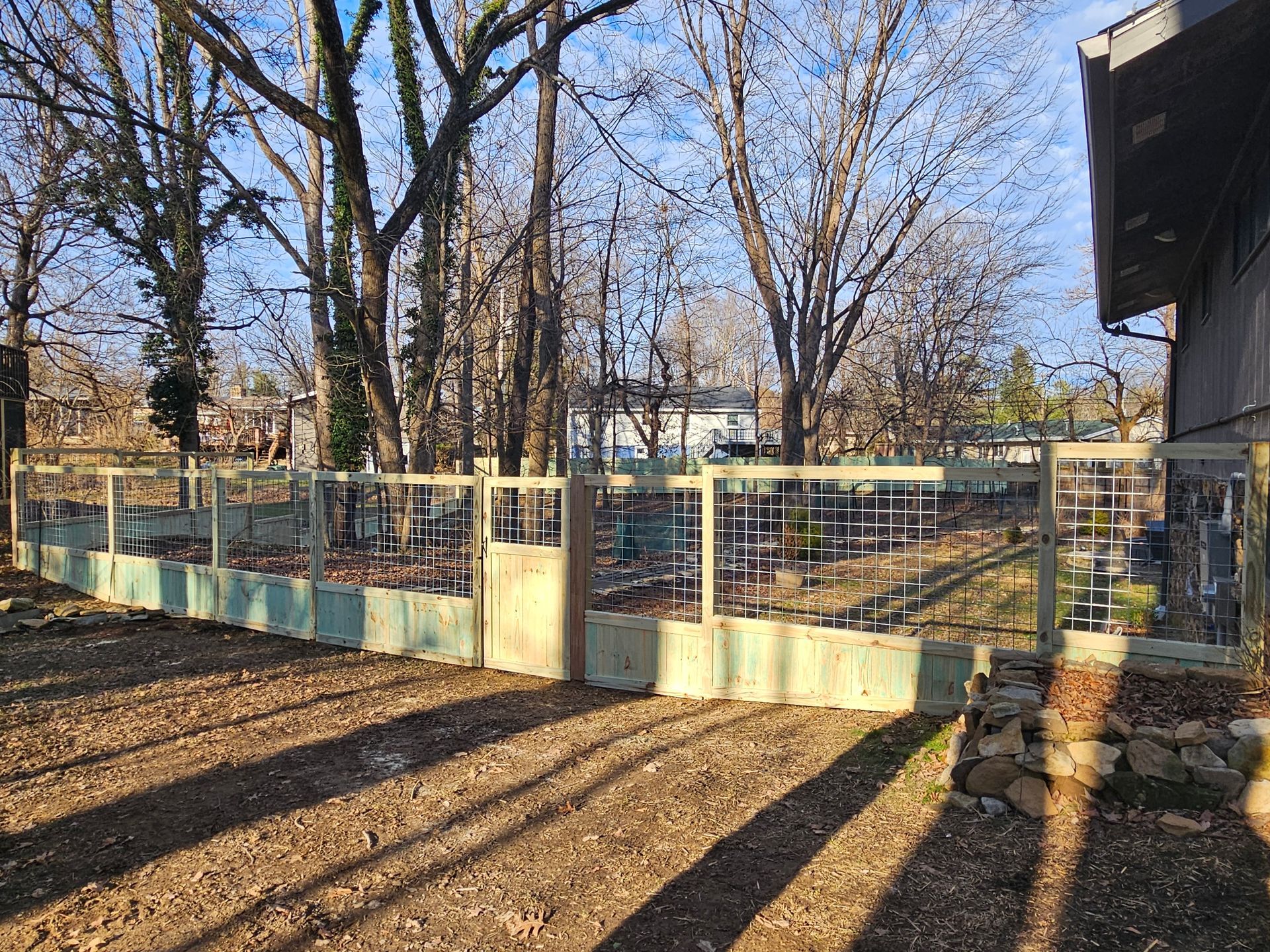 A wooden fence surrounds a yard with leafless trees under a bright sky.