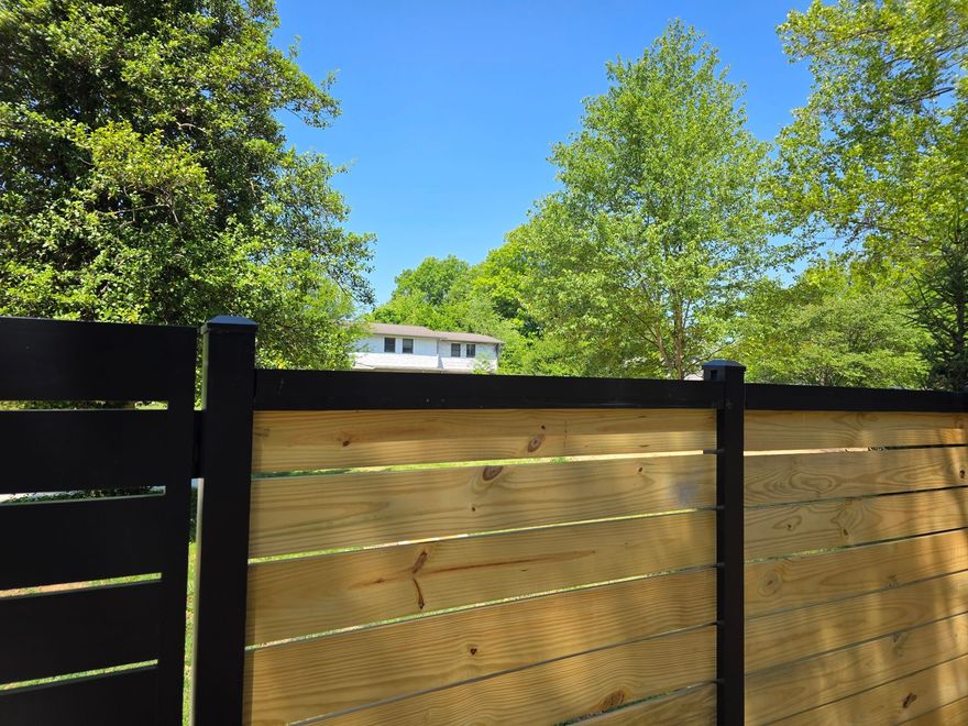 Wooden horizontal slat fence with black posts, bordering a grassy yard.