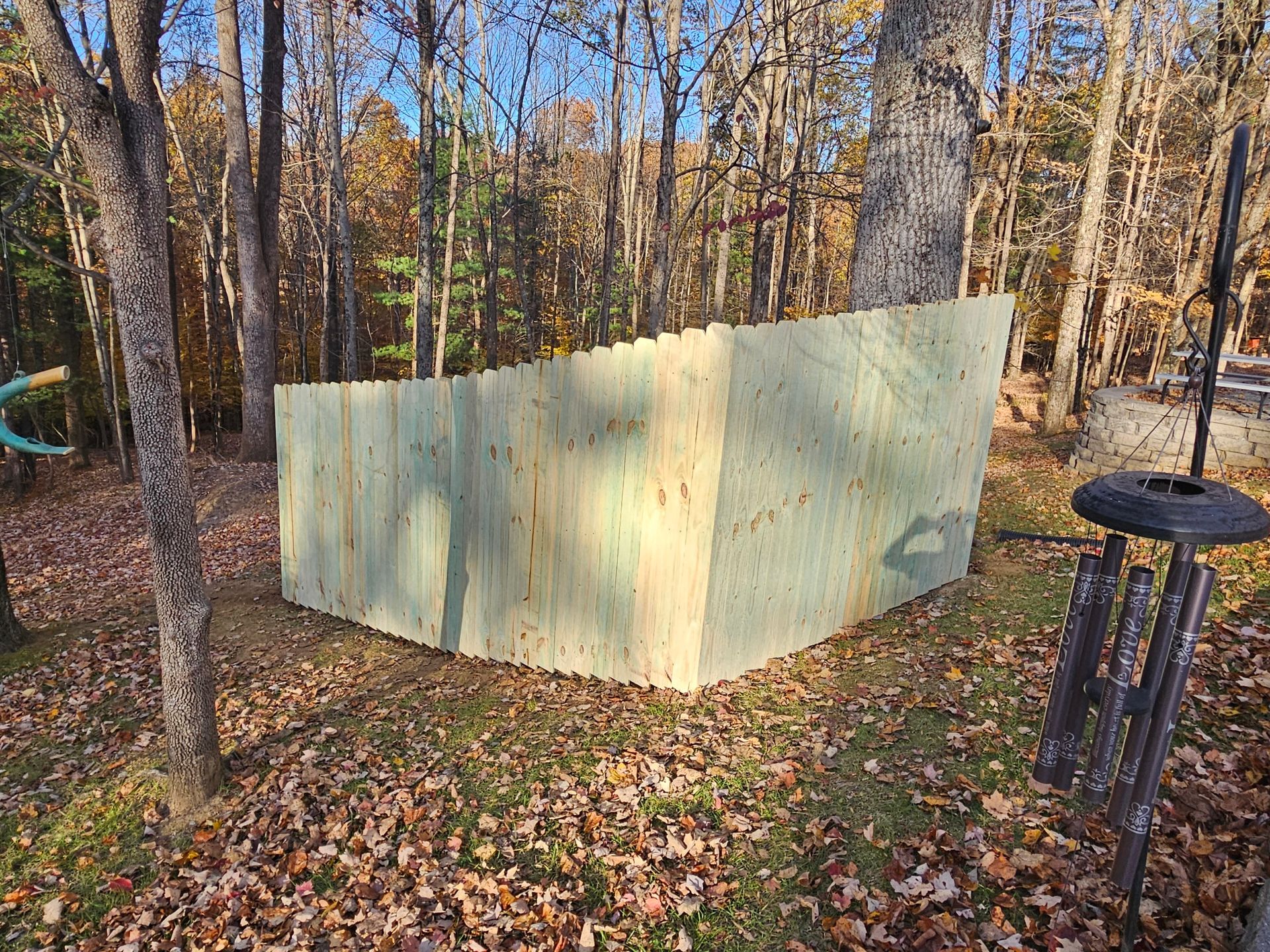 Wooden fence in a wooded area; leaves on the ground.