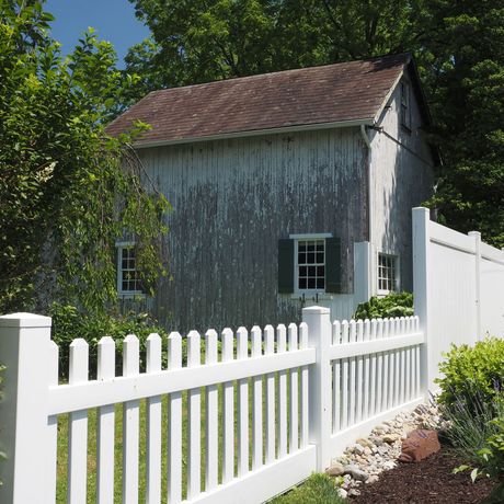 White porch with railing and gate next to a brick wall.