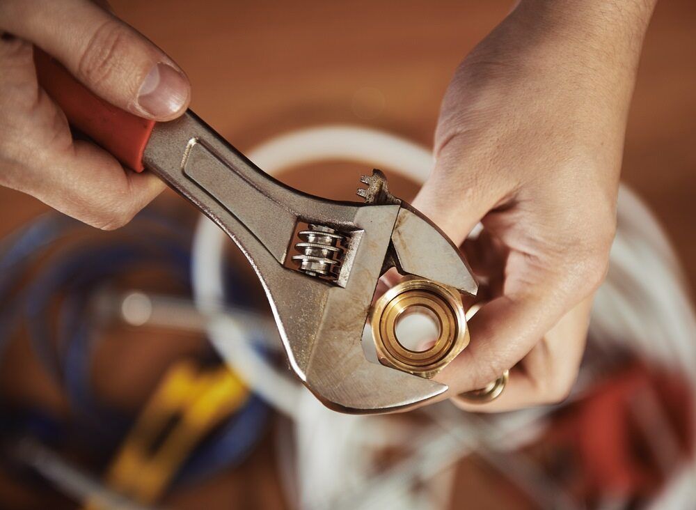 A Person Is Holding A Wrench Over A Brass Fitting — Bennett Plumbing In Broughton Village, NSW