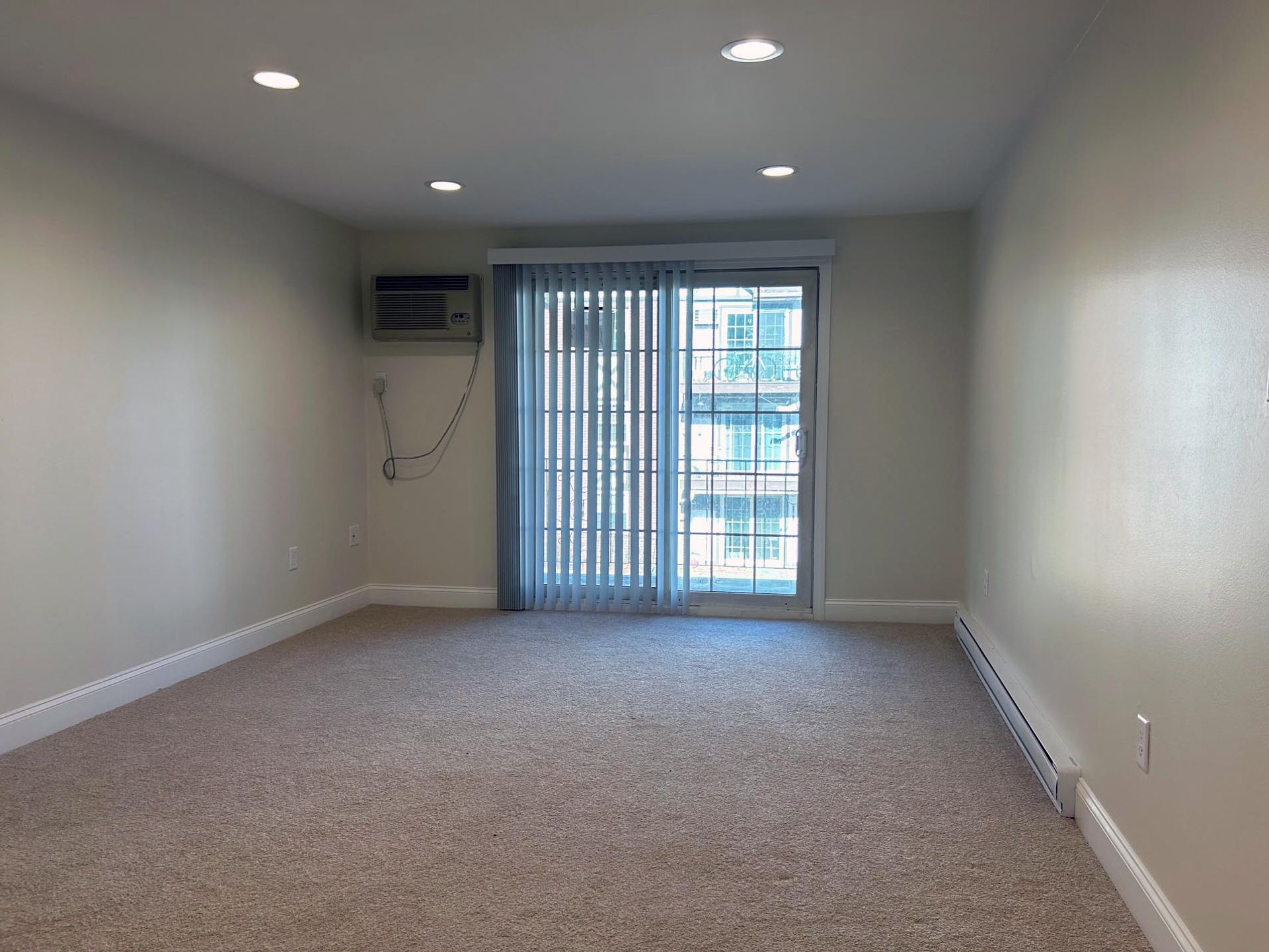 An empty living room with a sliding glass door and a window.