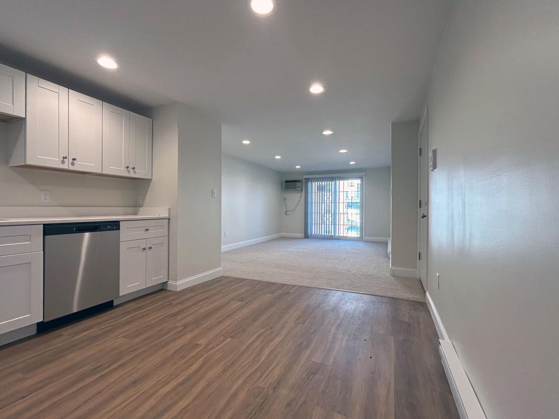 An empty apartment with a kitchen , living room , and stainless steel appliances.