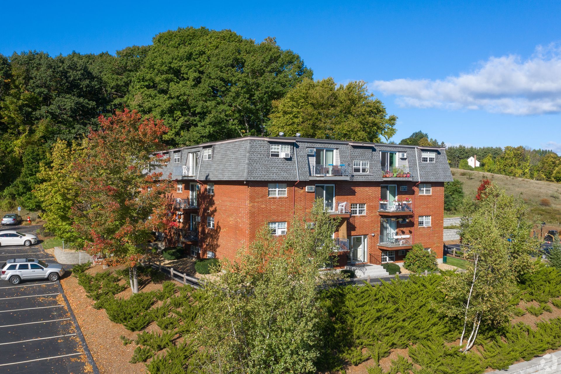 An aerial view of a brick apartment building surrounded by trees and a parking lot.