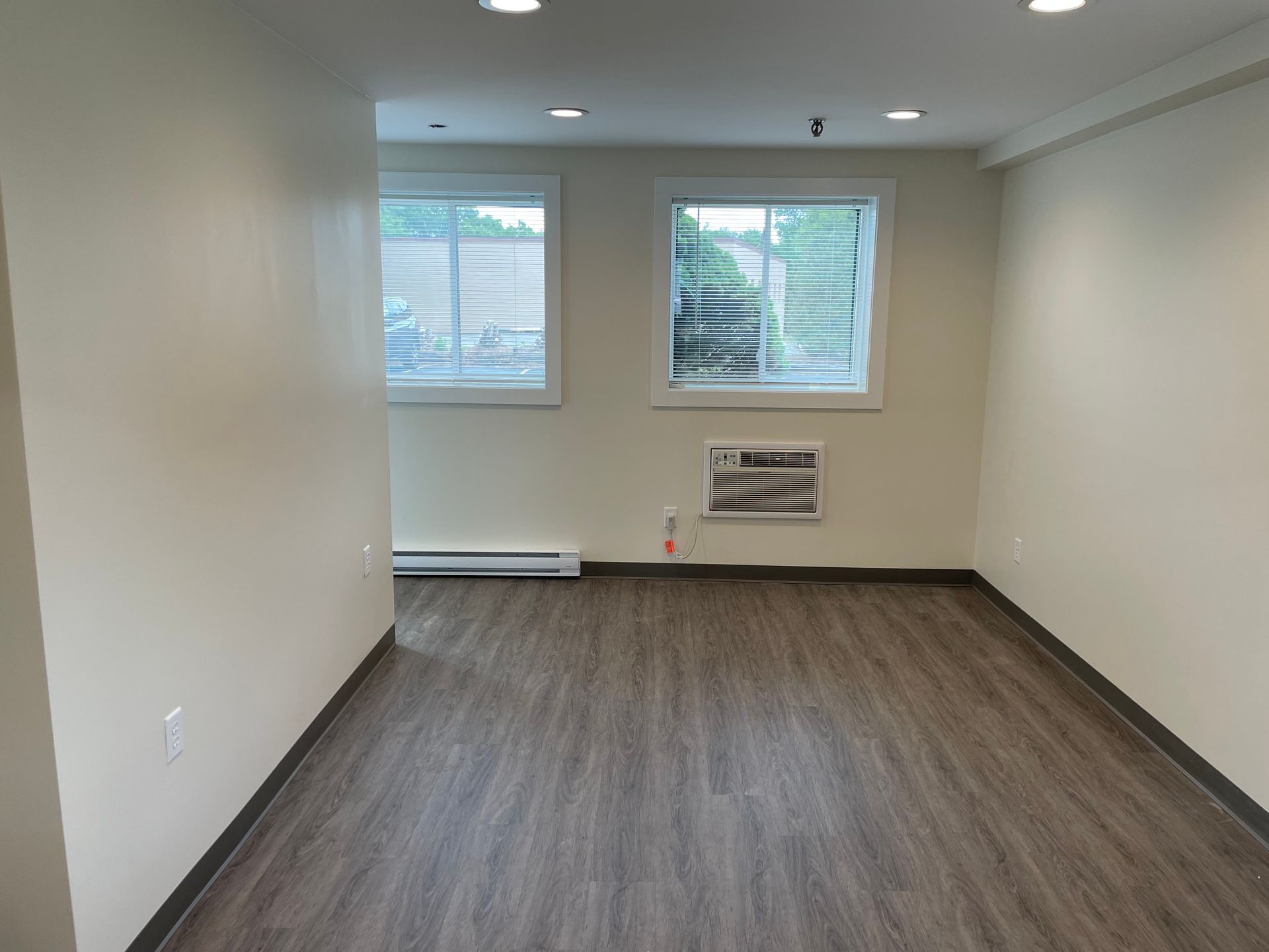 An empty room with hardwood floors and two windows