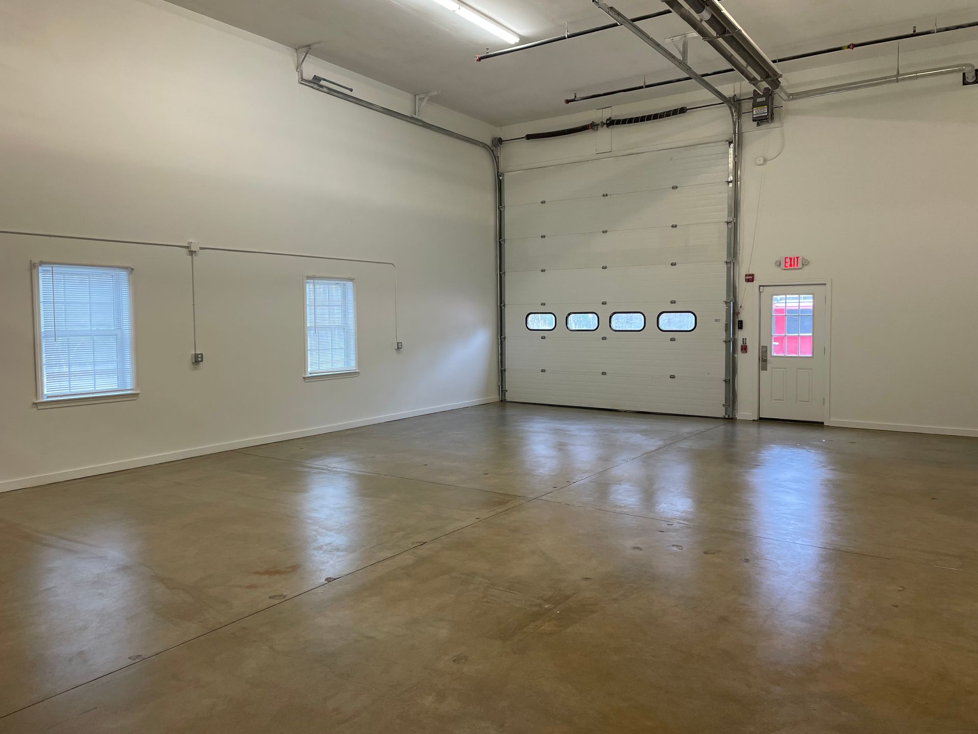 A large empty room with a garage door and windows.
