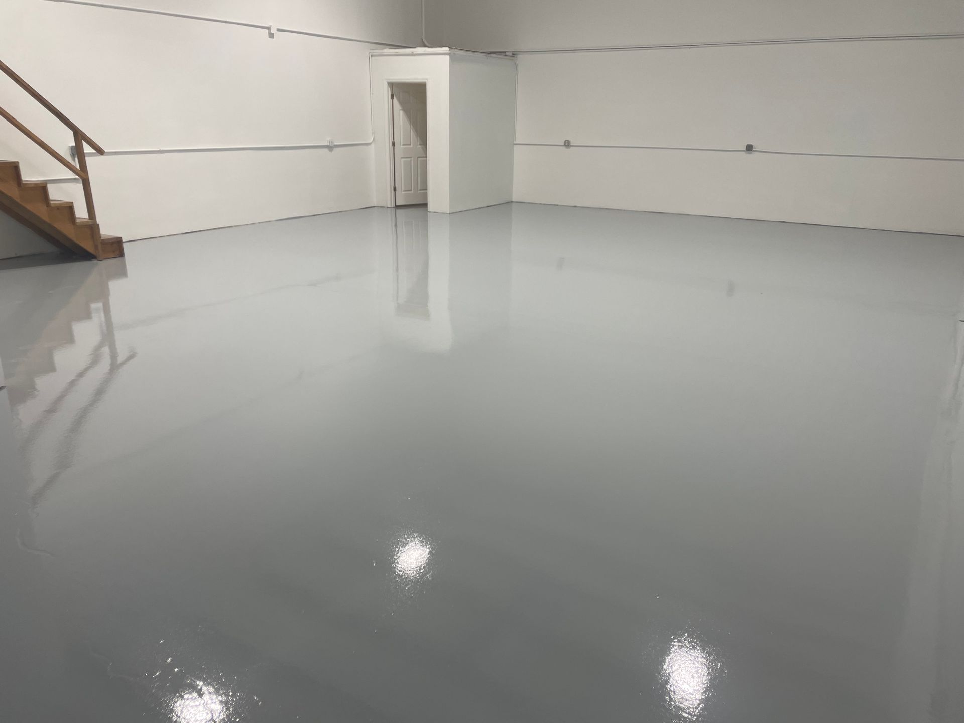 A large empty room with a staircase and a gray floor.