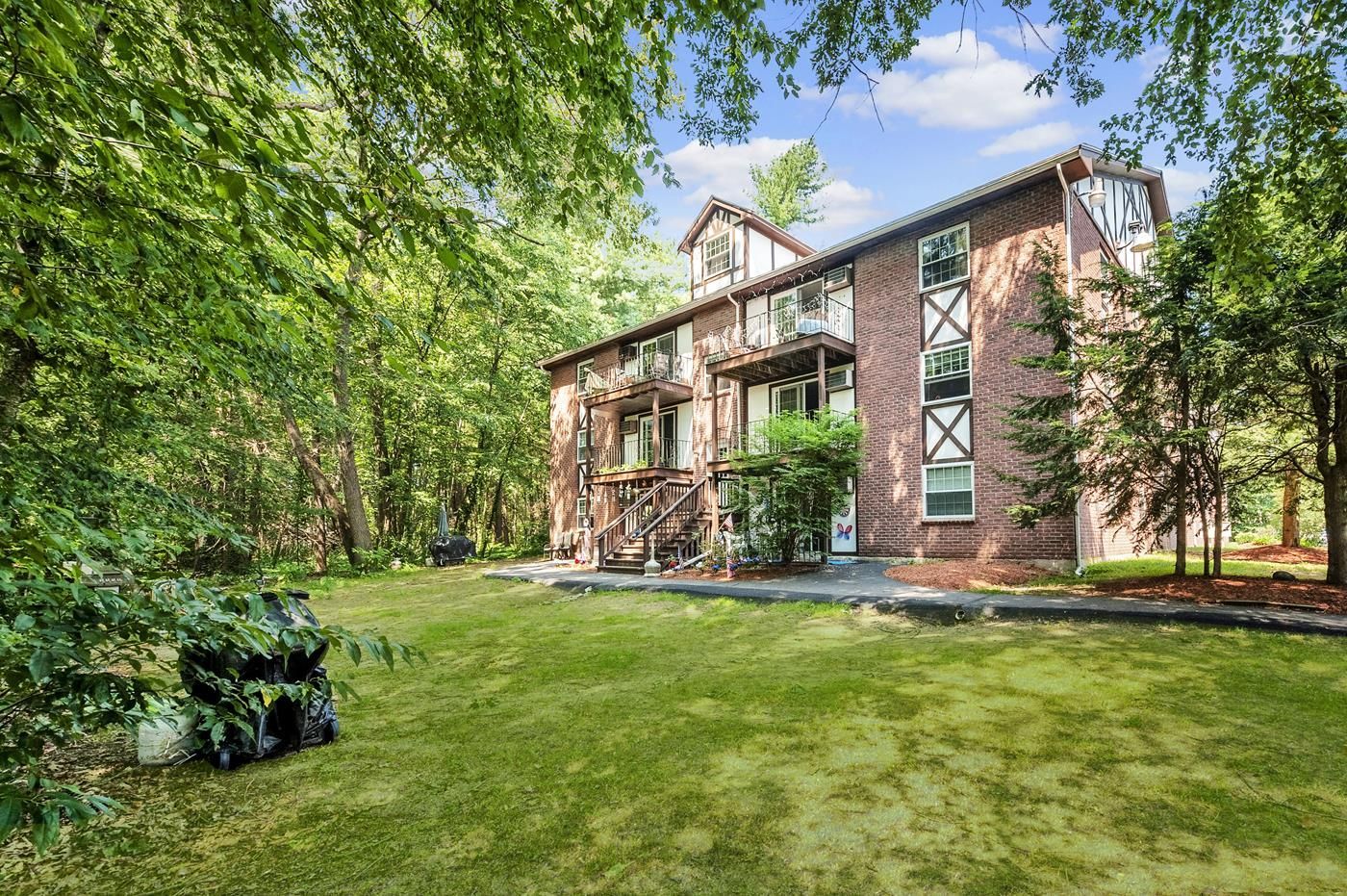 A large brick apartment building with a large lawn in front of it surrounded by trees.