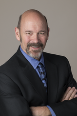 A man in a suit and tie is smiling with his arms crossed.