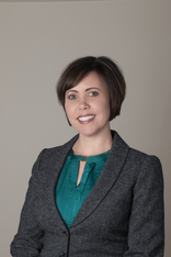 A woman in a suit and green shirt is smiling for the camera.