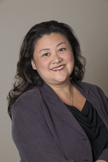 A woman in a purple jacket and black shirt is smiling for the camera.