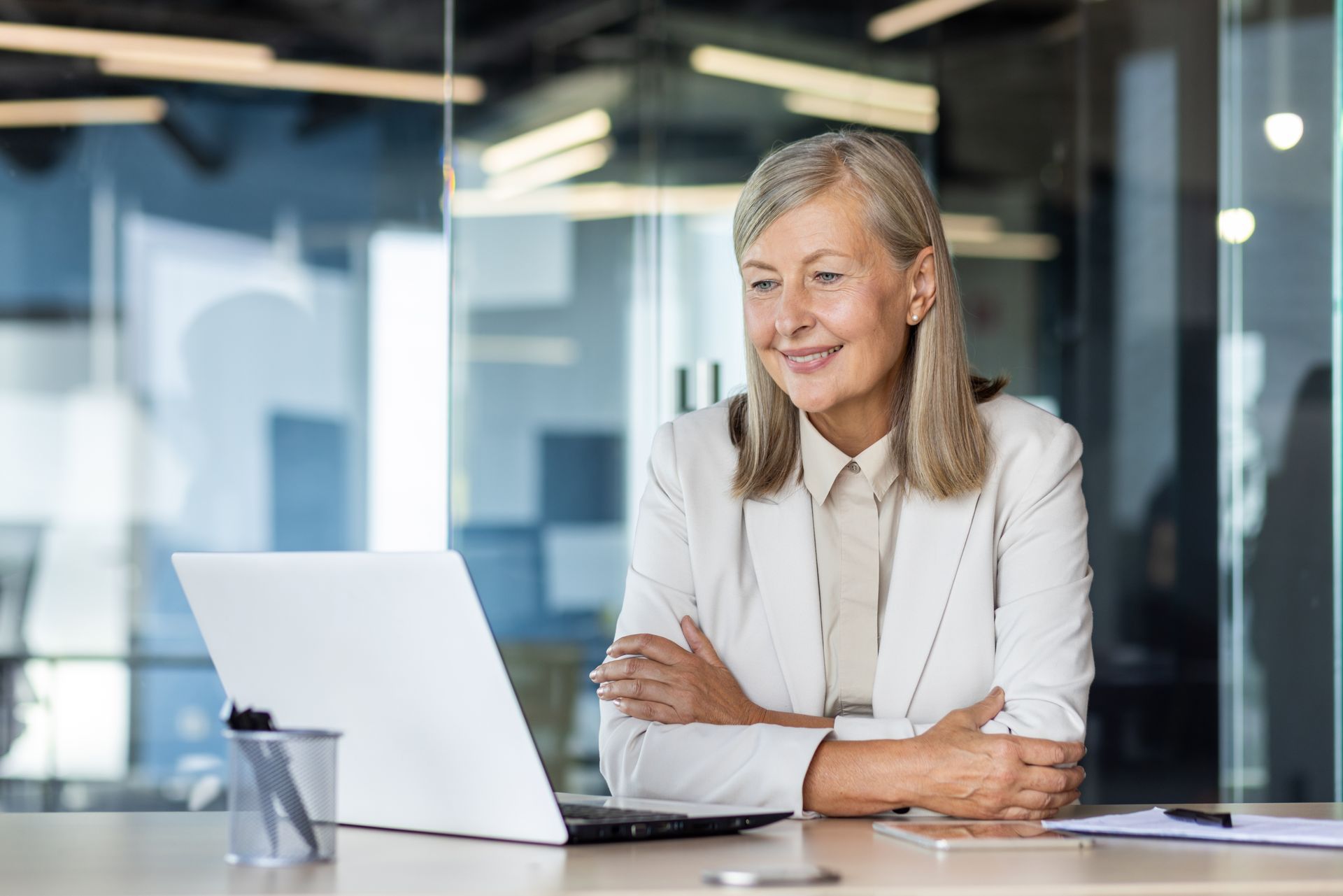 a woman sits at a desk with her arms crossed in front of a laptop