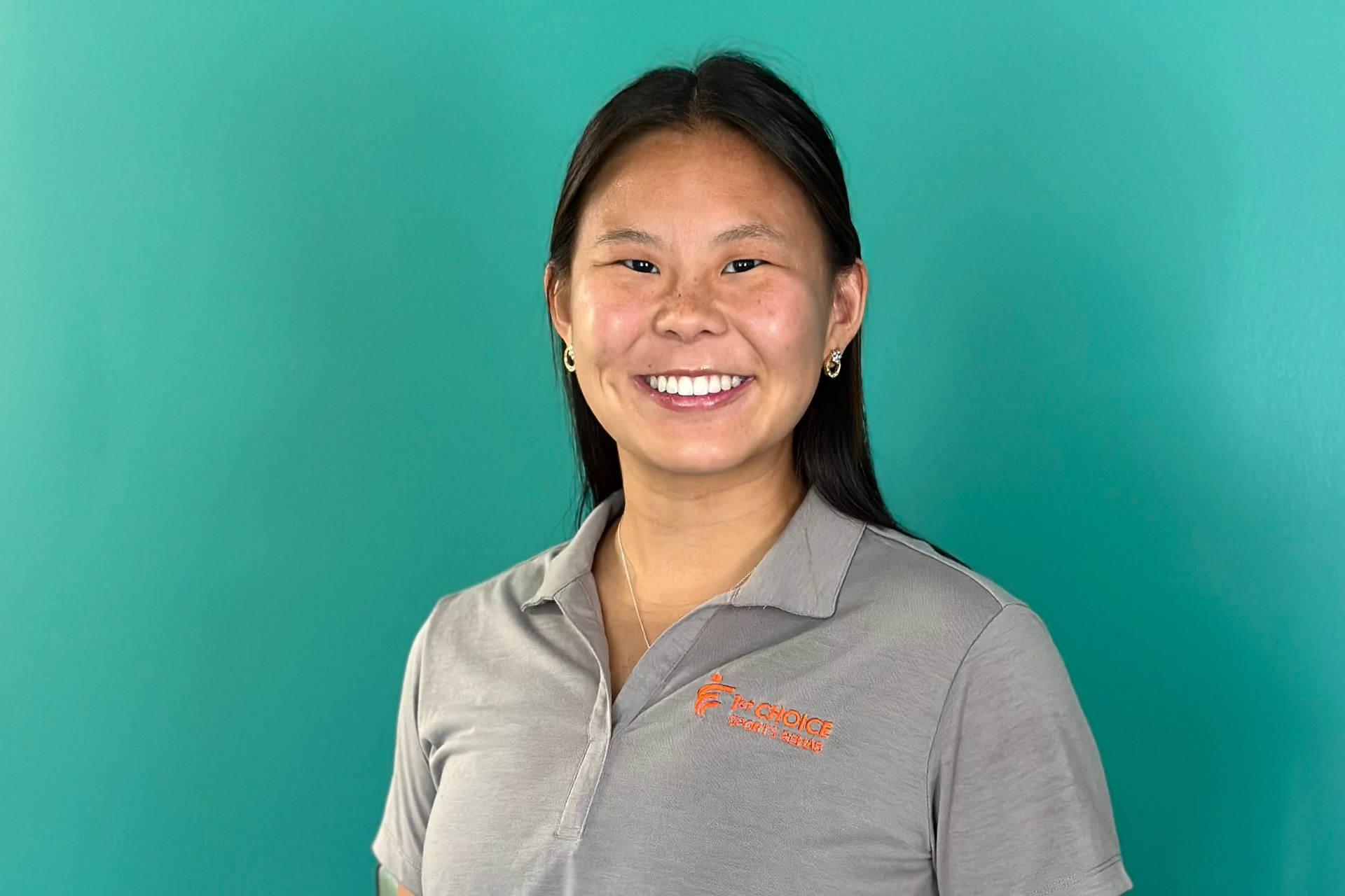 A smiling person in a gray polo stands against a teal background.