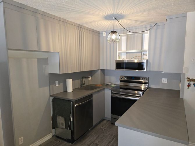 Cuisine moderne avec placards gris, appareils électroménagers noirs et luminaire central.