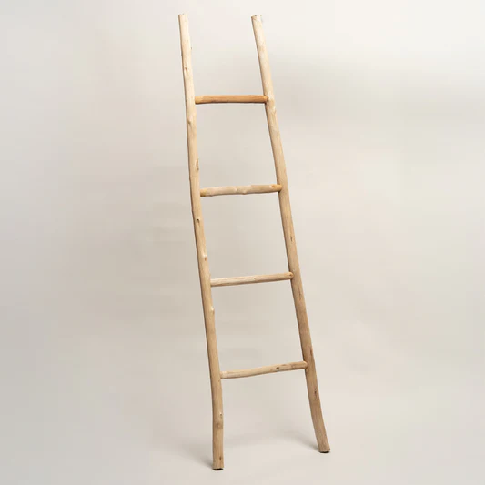 Una escalera decorativa rústica de madera de color claro apoyada contra una pared blanca lisa.