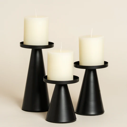 Tres candelabros negros en forma de cono, de diferentes alturas, cada uno rematado con una vela cilíndrica blanca y gruesa.